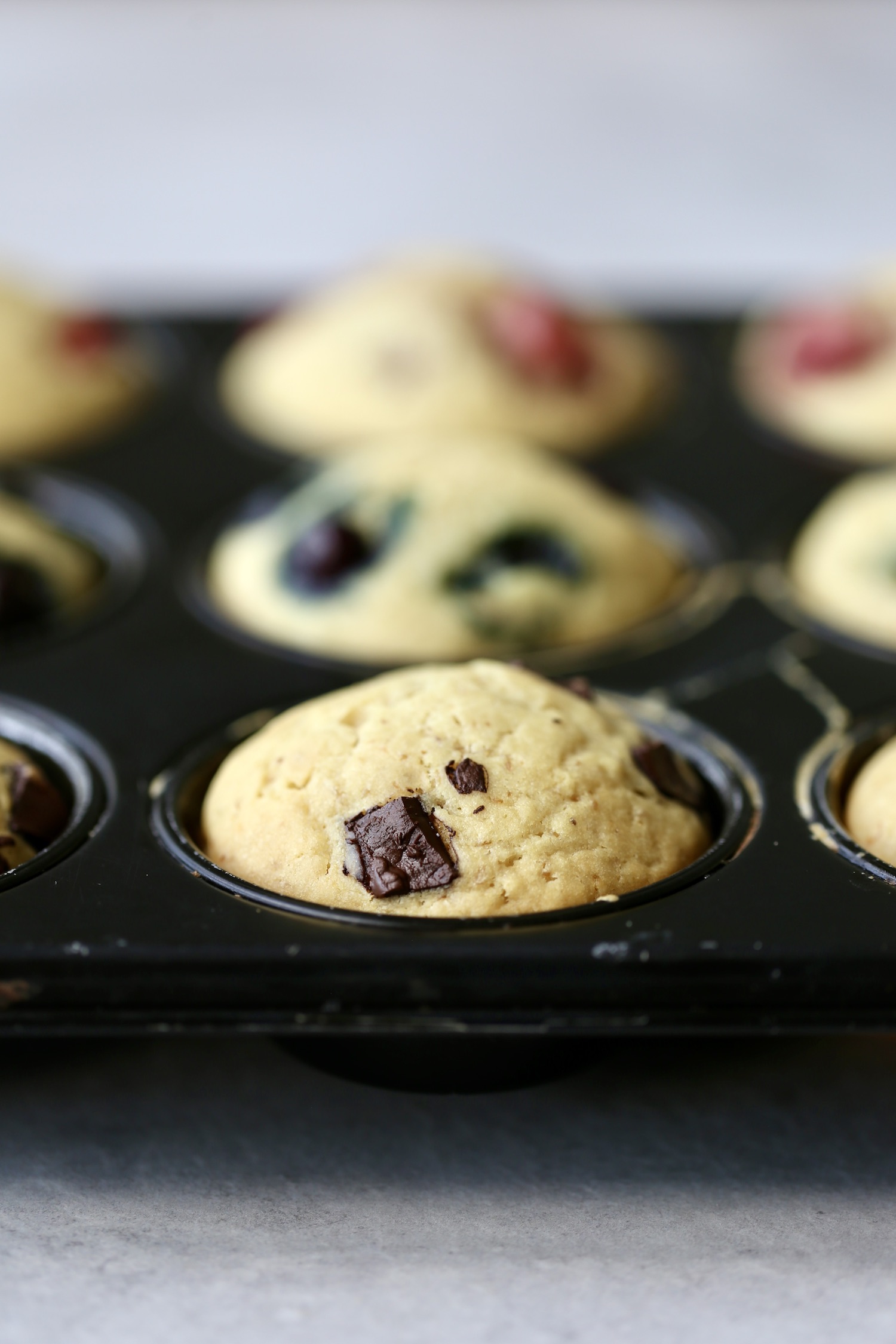 Chocolate chip, blueberry and strawberry sourdough muffins lined up in a muffin tin. 