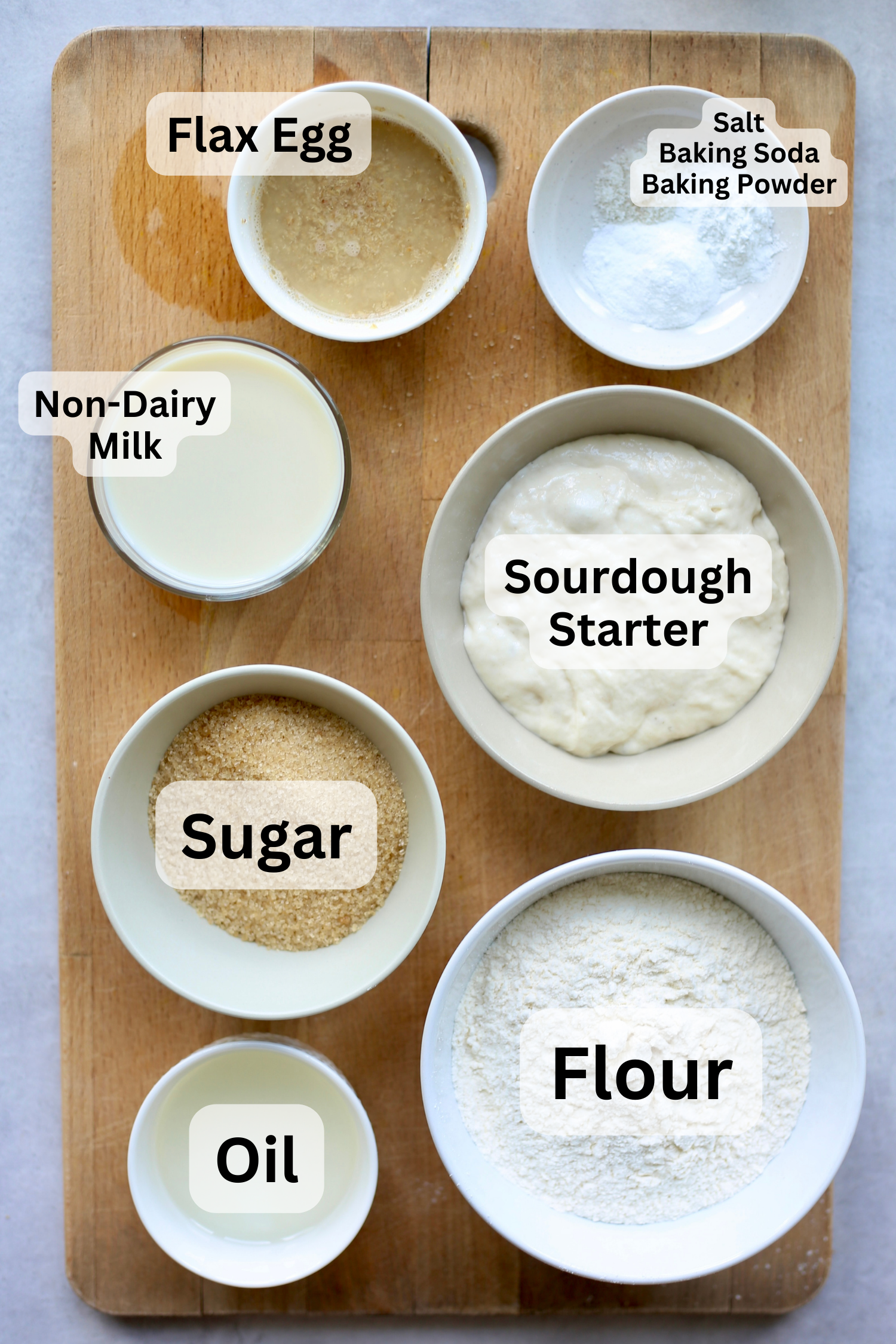 All of the ingredients for sourdough muffins measured out into bowls on a wooden cutting board. 