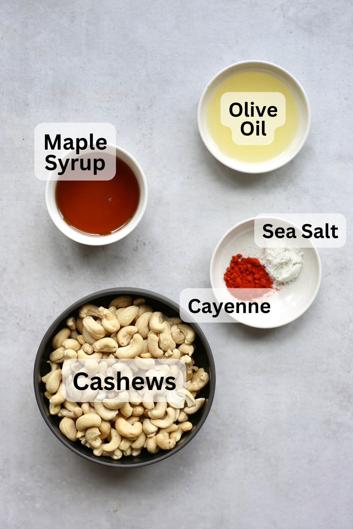 Cashews, maple syrup, olive oil, cayenne and sea salt measured out into bowls on a table.