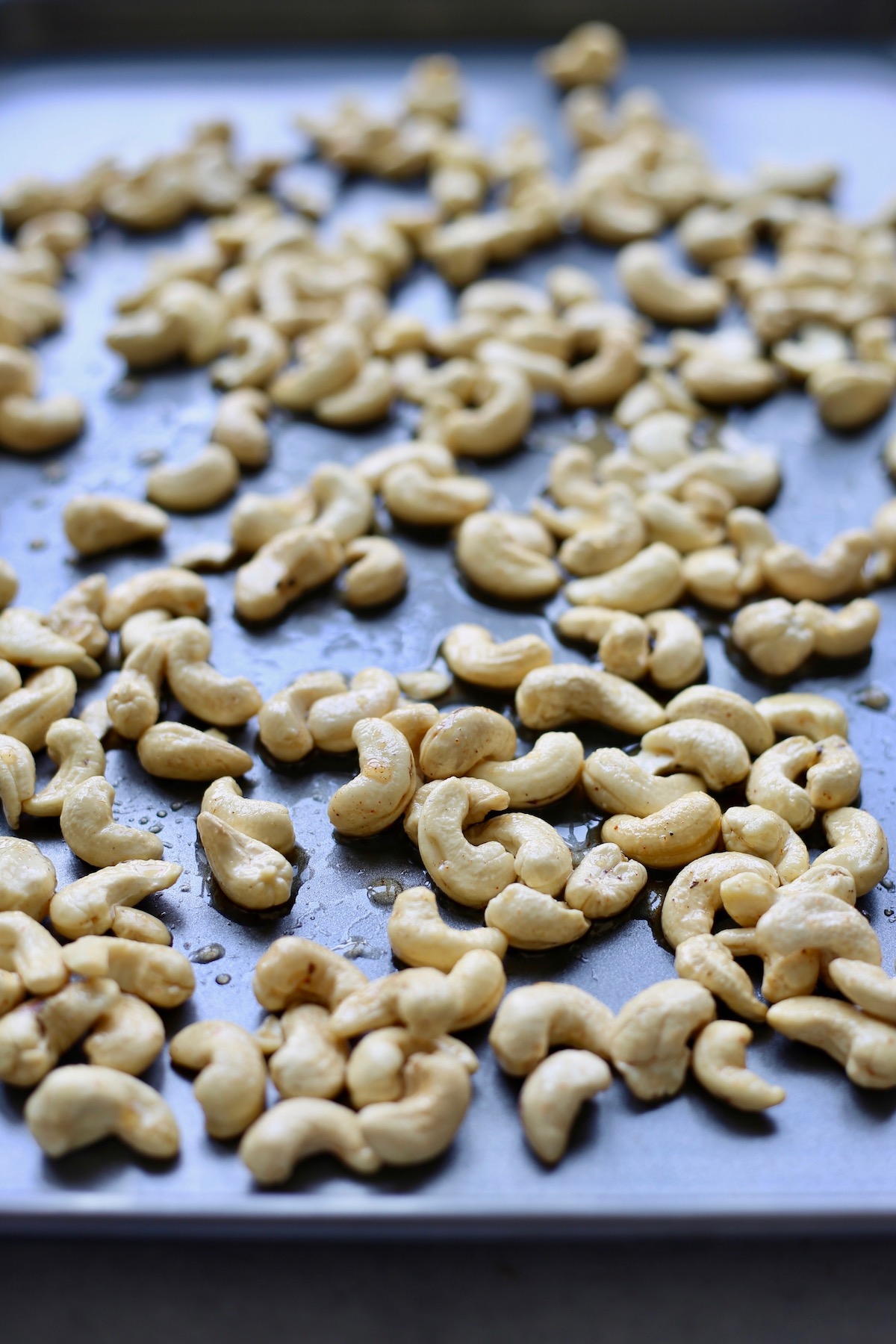 Raw cashews coated in oil and maple syrup on a baking sheet.