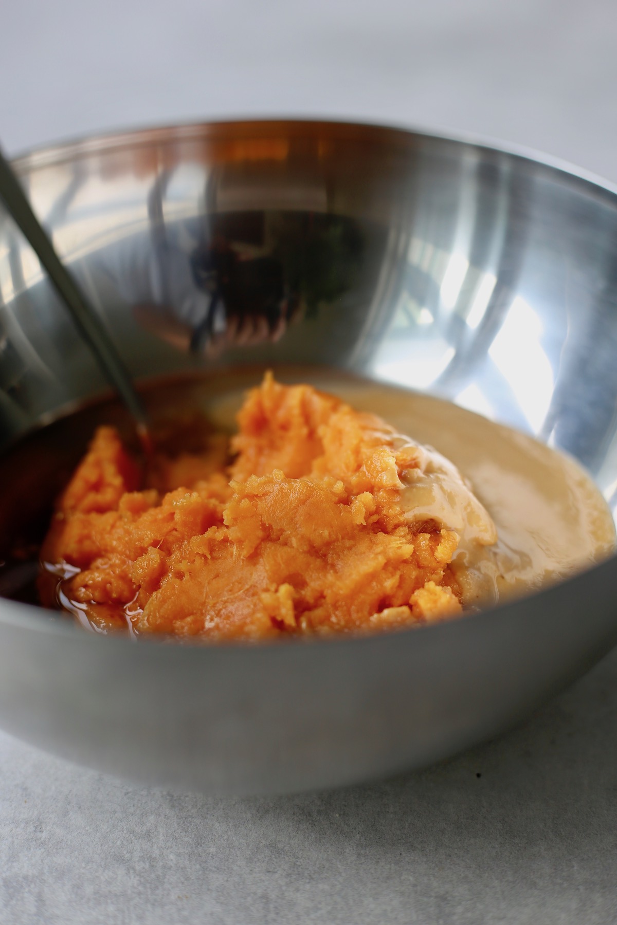 Mashed sweet potato, almond butter and maple syrup in a large mixing bowl.