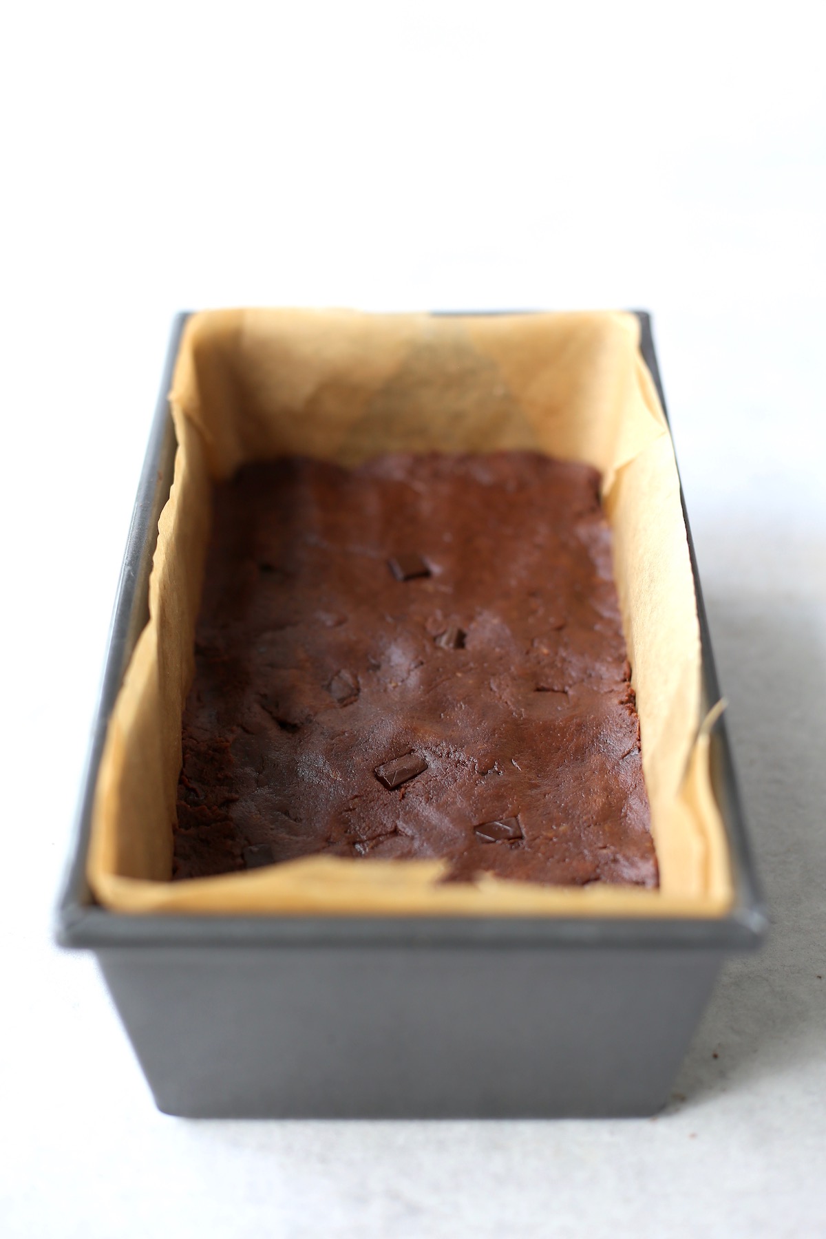 A loaf pan lined with parchment paper and sweet potato brownie batter.
