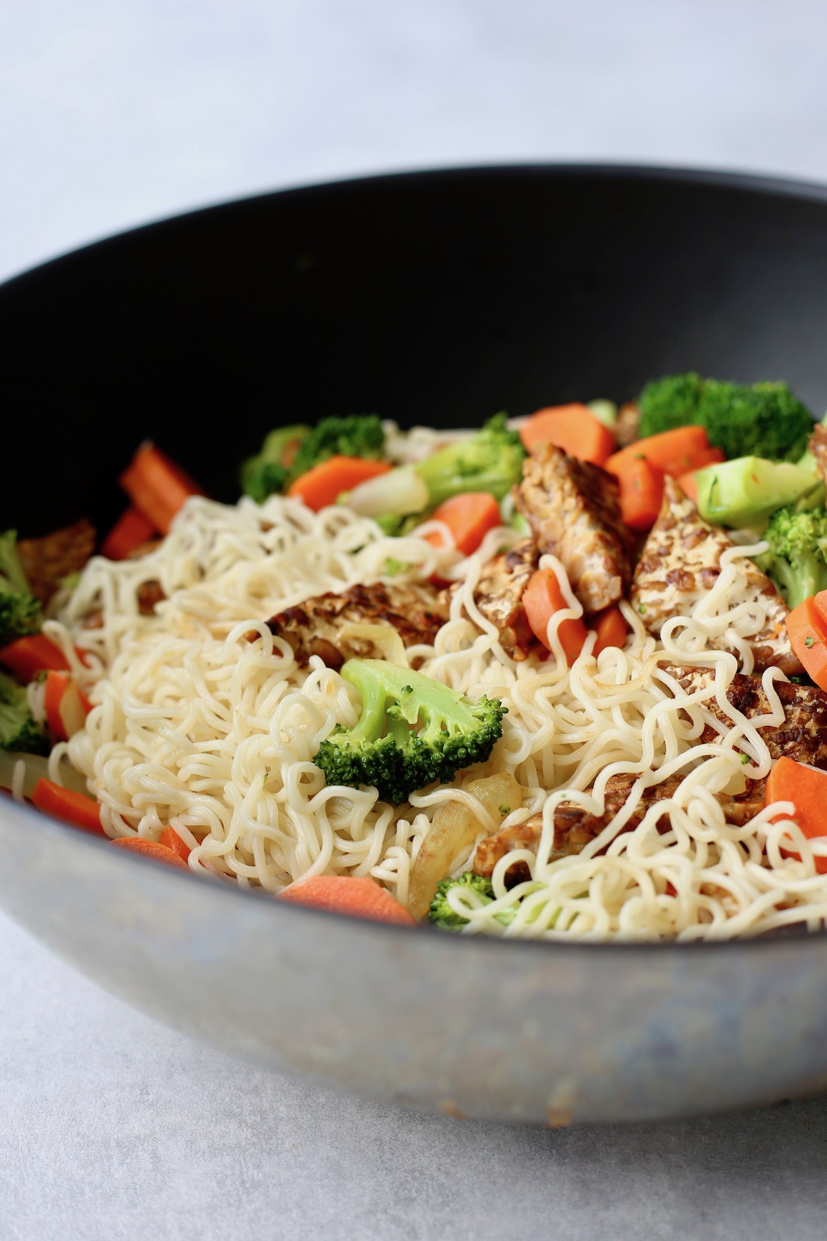 Plain cooked noodles, broccoli, carrots and tempeh in a large wok. 