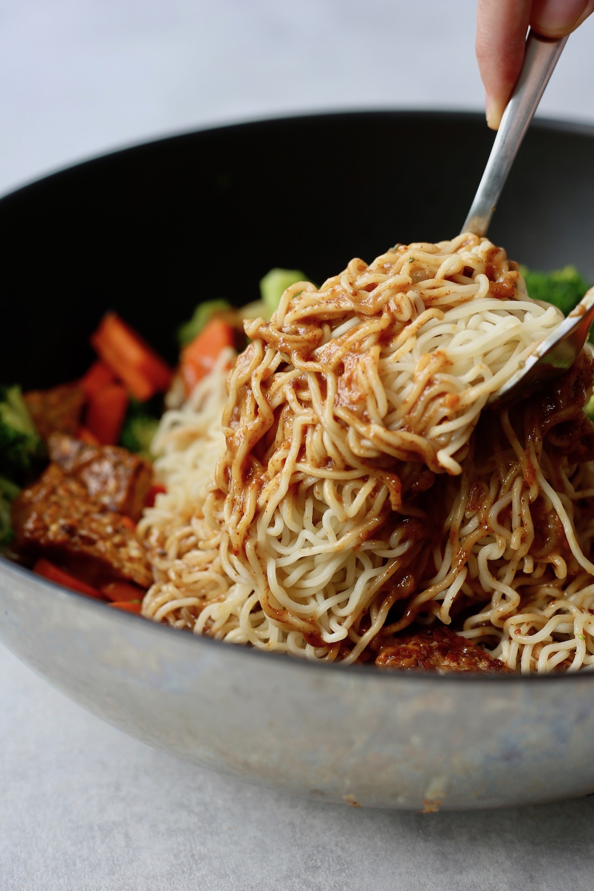 Almond butter sauce being tossed with soba noodles to create a rich vegan soba noodle recipe with veggies and tempeh. 