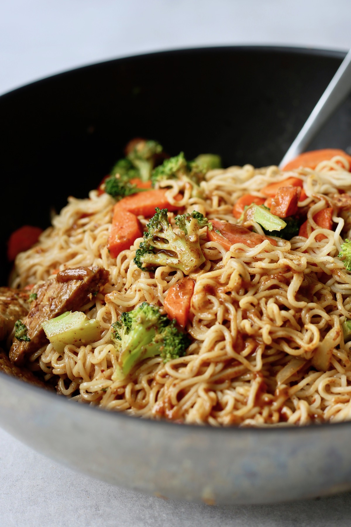 A big black wok full of saucy noodles, broccoli, carrots and tempeh. 