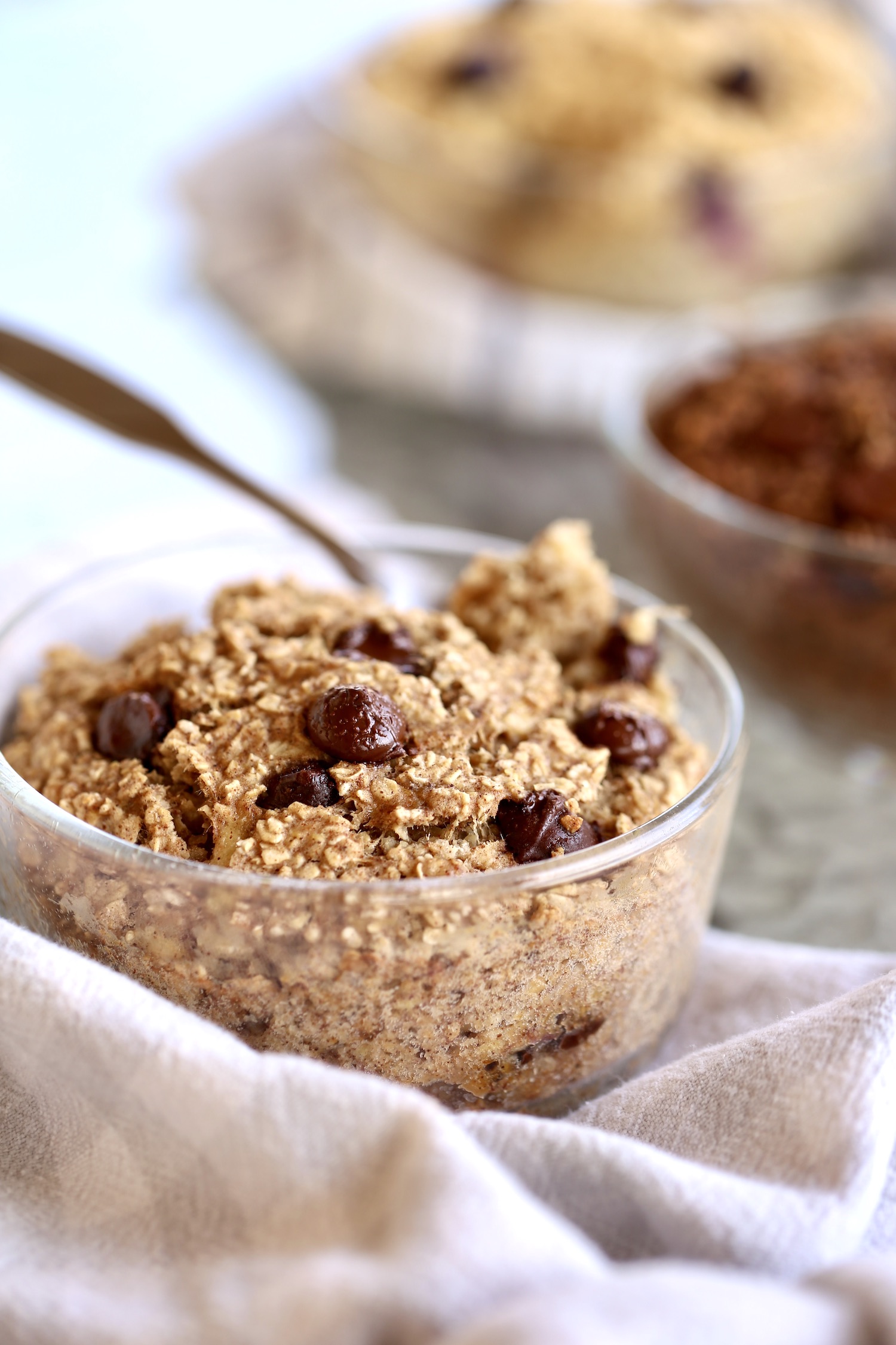 A single serving of banana bread baked oatmeal in a glass baking dish on a towel with chocolate chips on top.