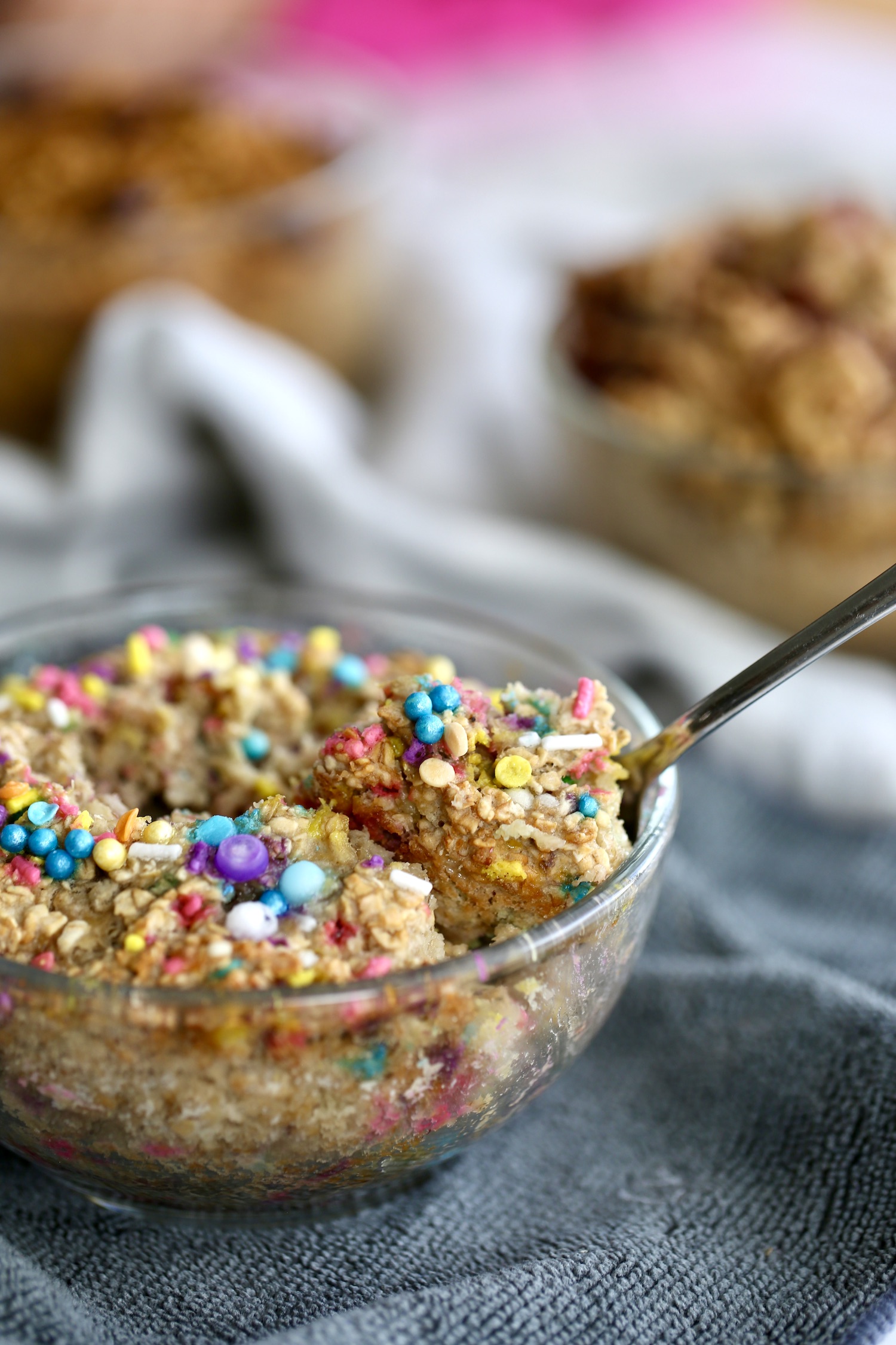 A close-up of a spoon scooping up birthday cake baked oatmeal with sprinkles on top.