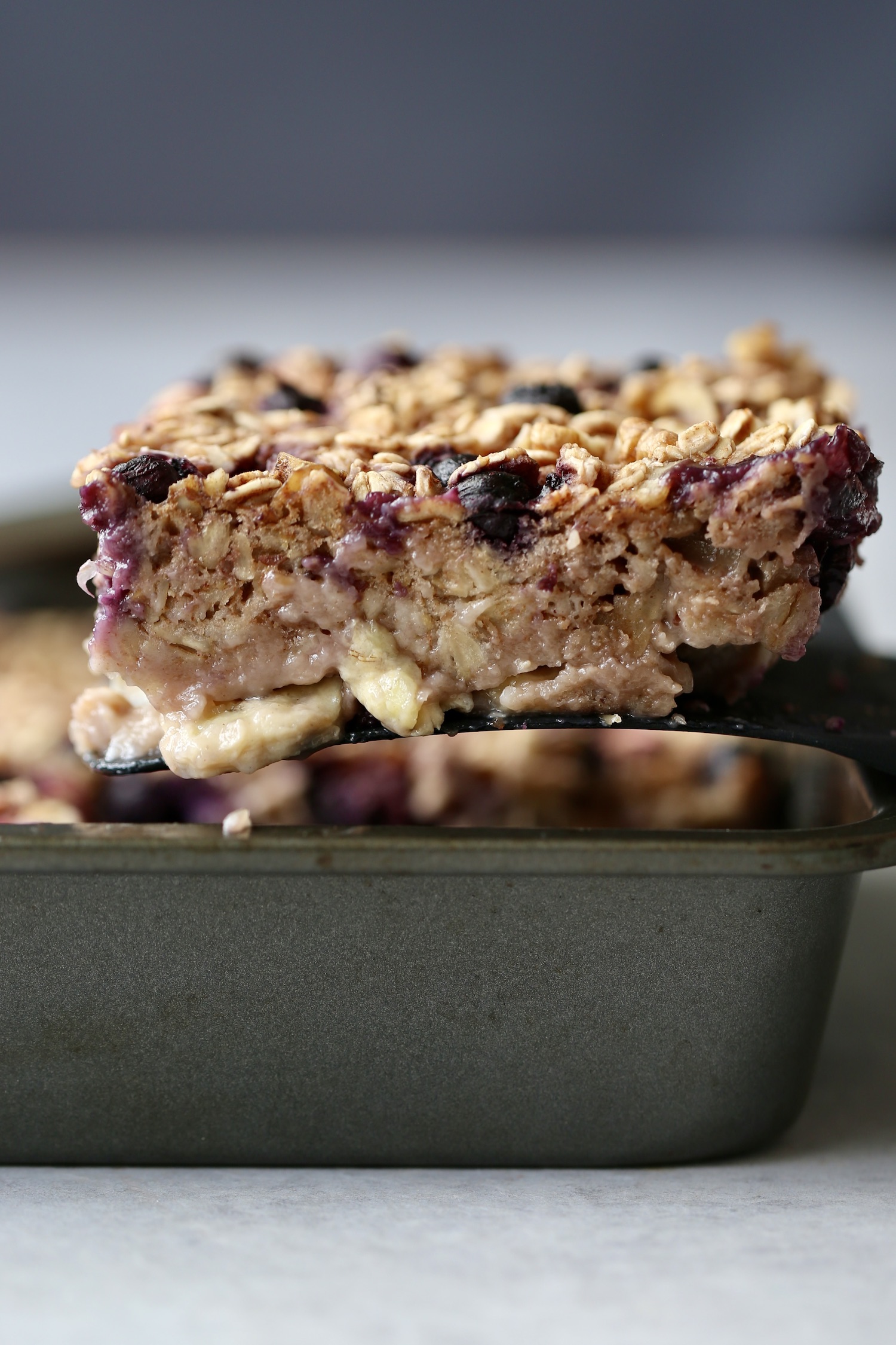 a thick slice of berry baked oatmeal being scooped out of a baking dish