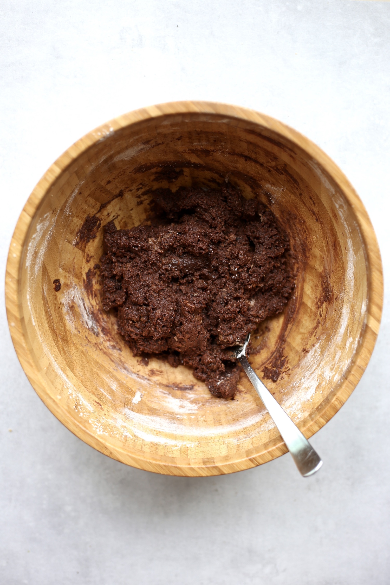 Vegan brownie batter being stirred together with a matal spoon in a large wooden mixing bowl. 
