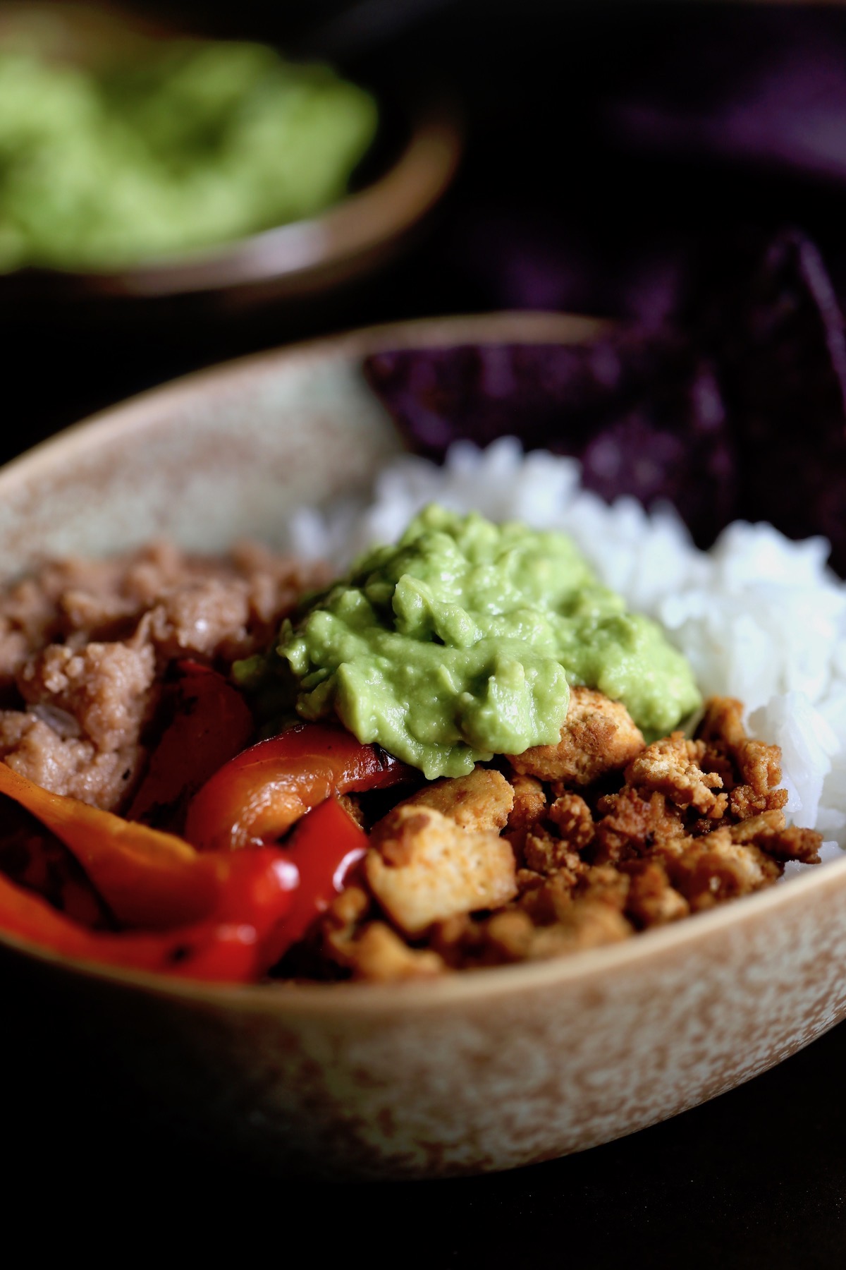 a vegan burrito bowl loaded with white rice, refried beans, taco tofu crumbles, sauteed peppers and homemade guac