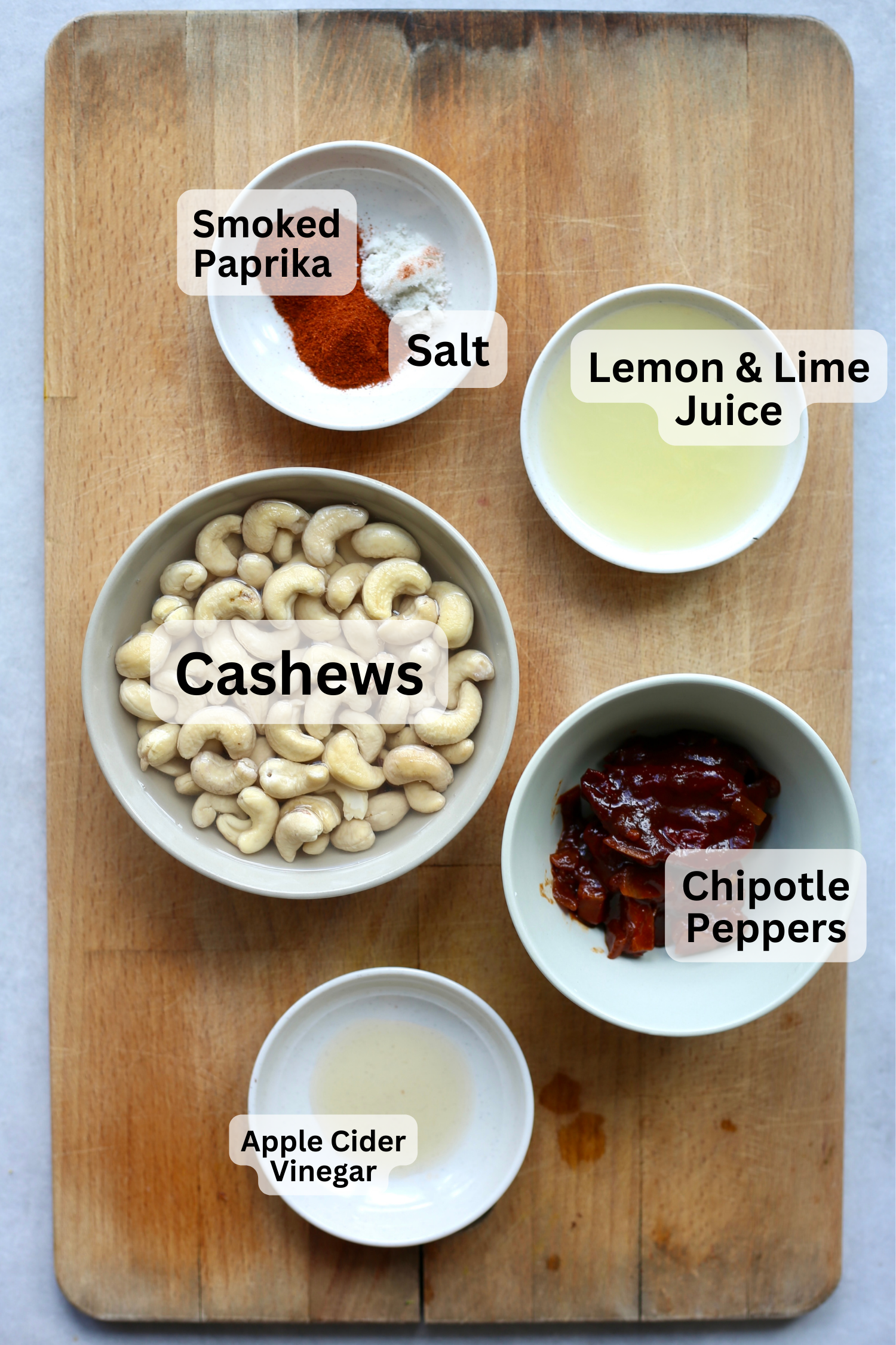 All of the ingredients needed for vegan chipotle mayo measured out into bowls and laid out on a wooden cutting board. 