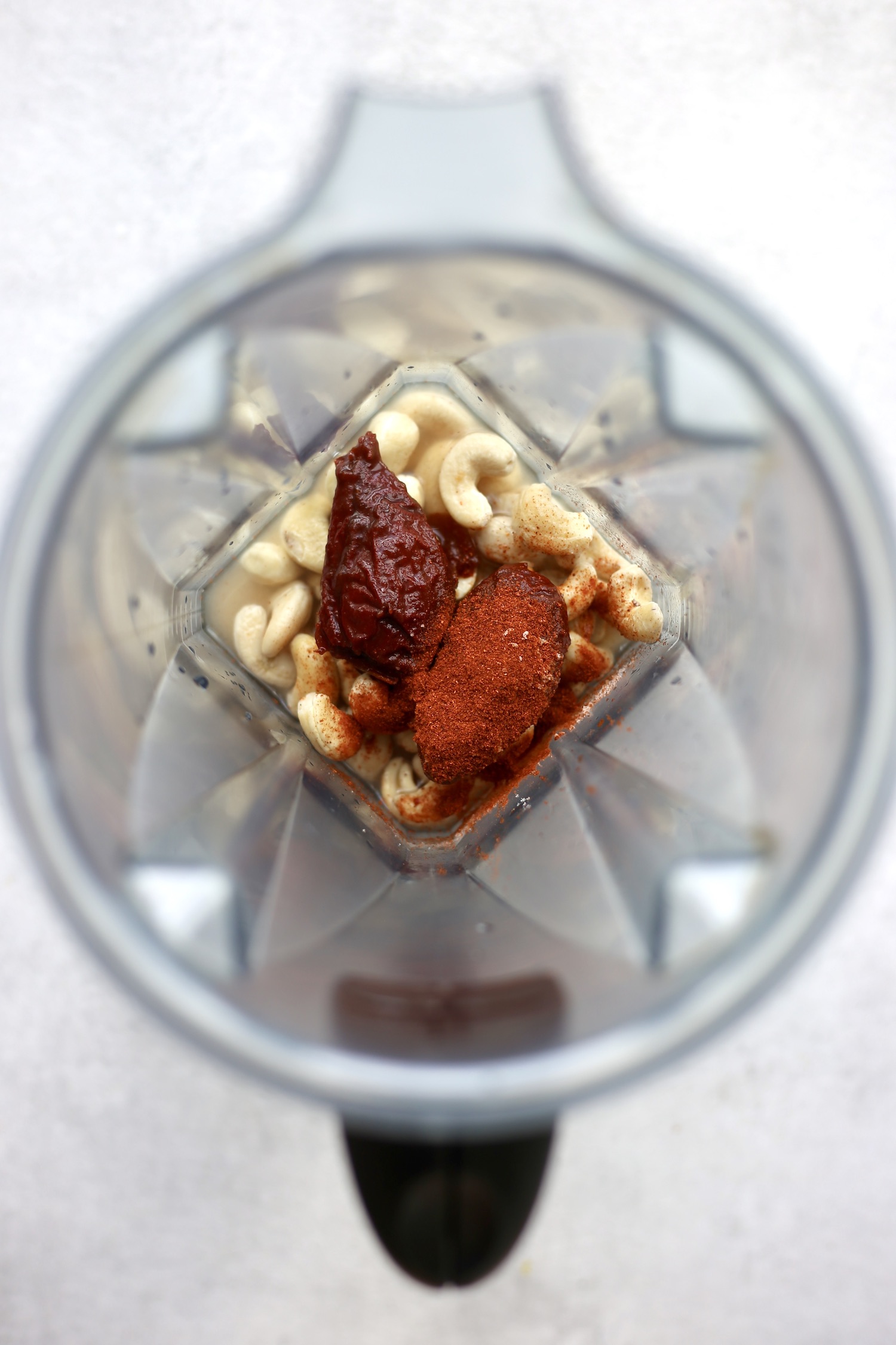 An above shot of a high speed blender filled with cashews chipotle peppers and smoked paprika. 