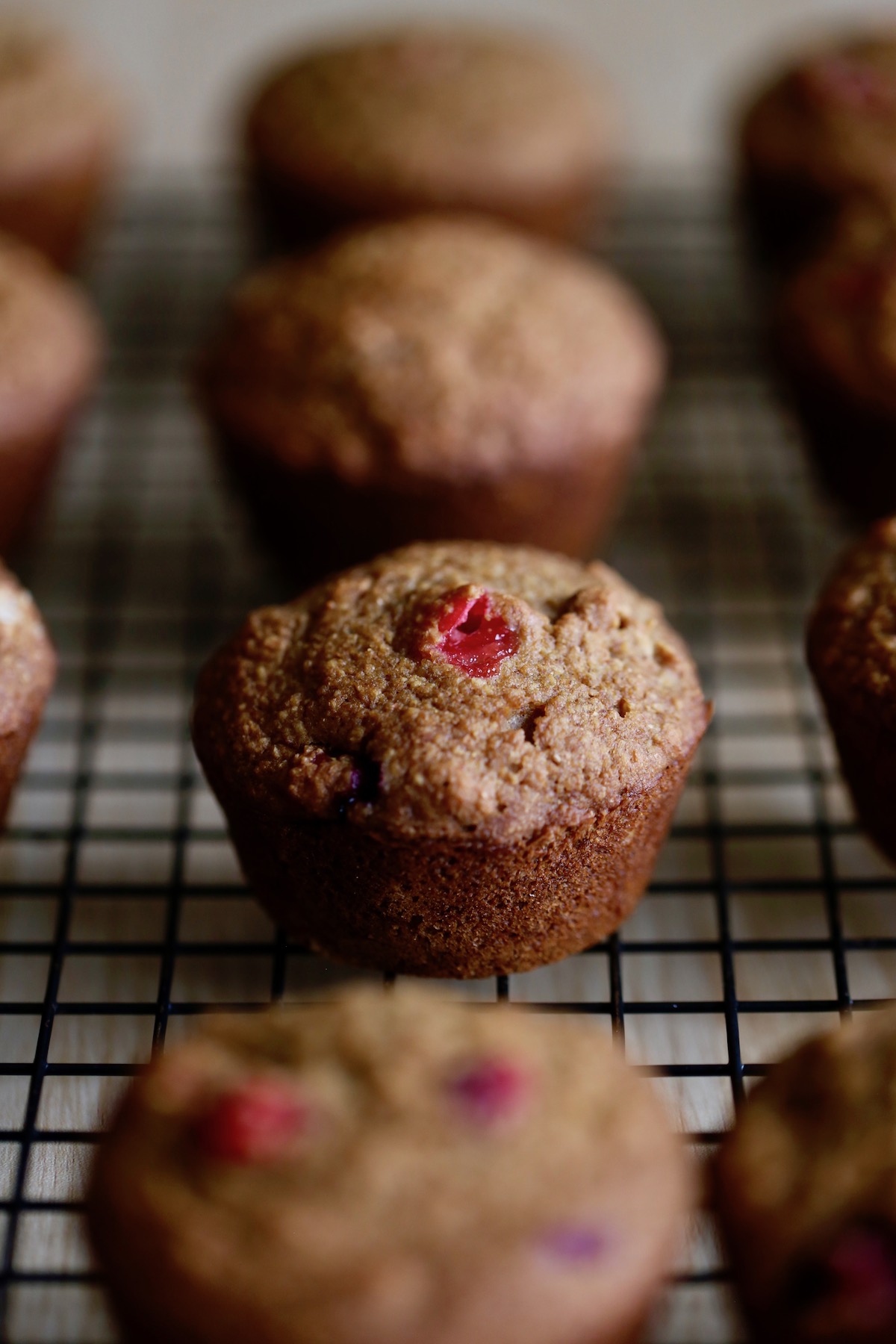 a juicy cranberry poking out of the top of a muffin on a cooling rack