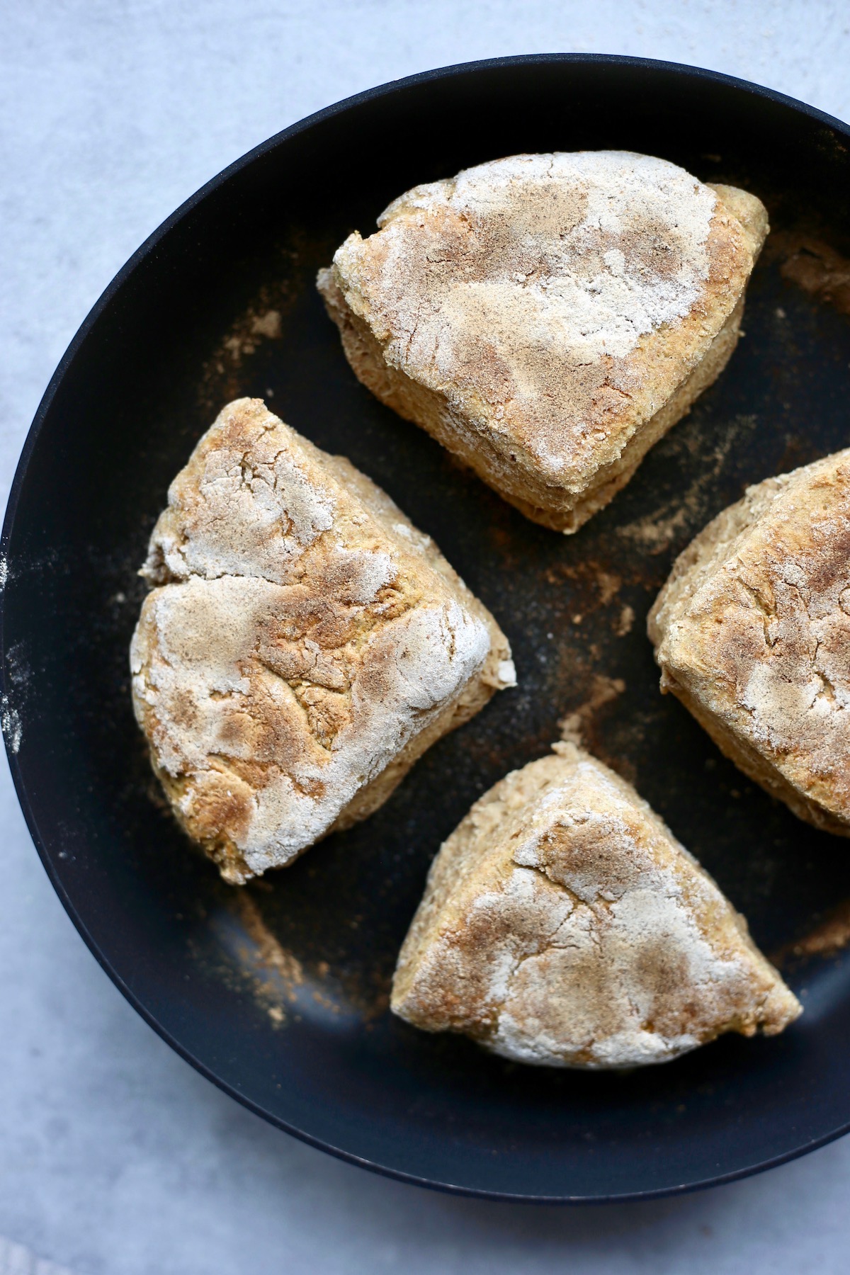 4 vegan Irish soda farls cooking on a hot skillet until golden brown