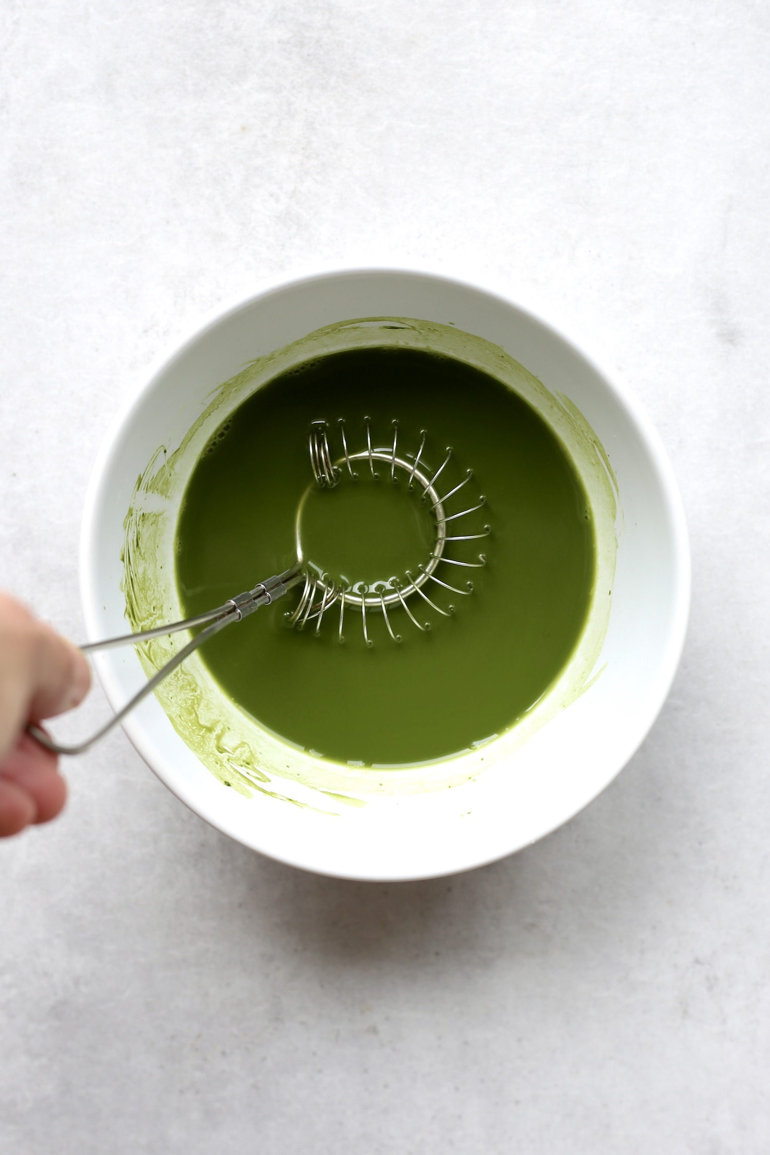 A circular whisk mixing matcha powder and hot water together in a bowl. 