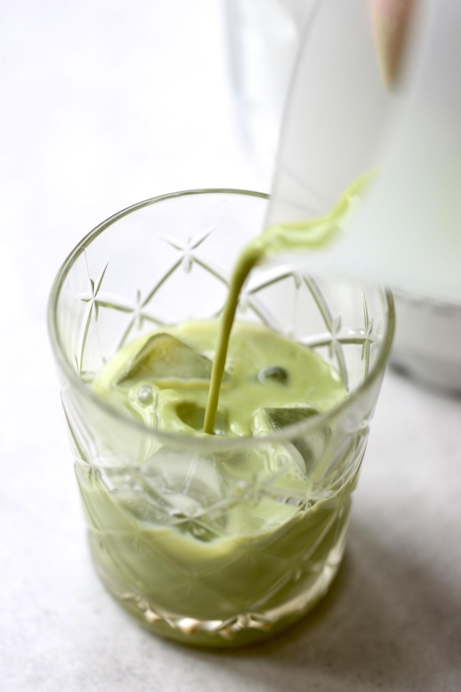 A dairy-free matcha latte being poured over ice in a glass. 