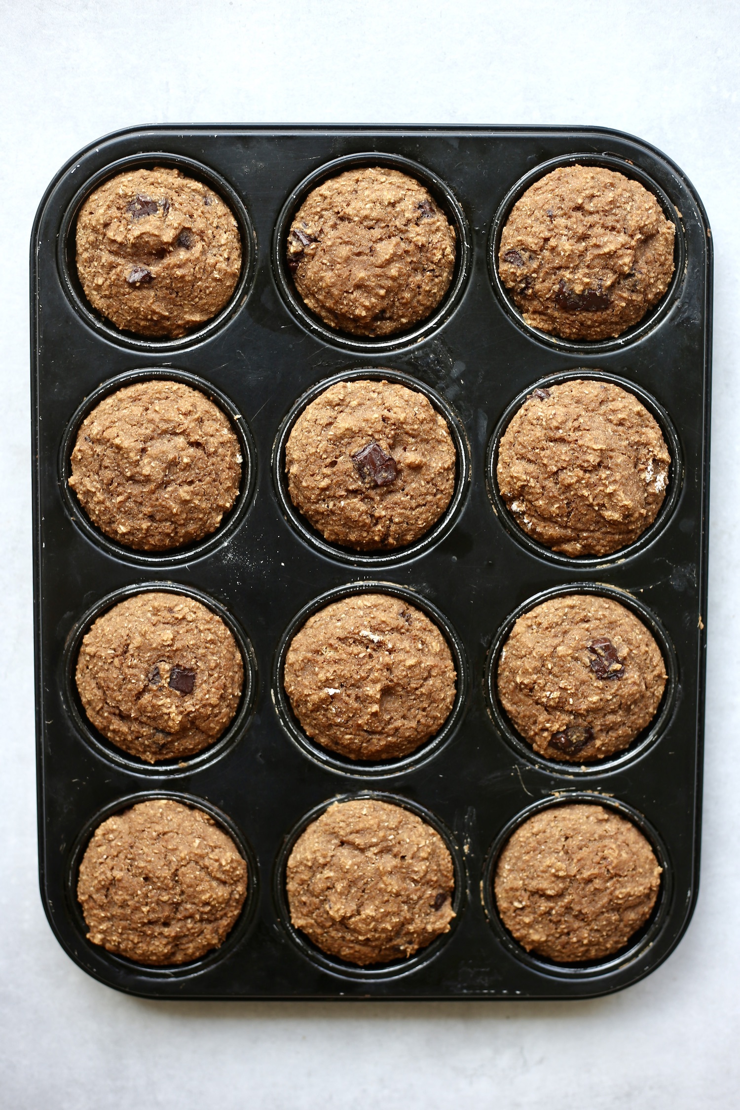 12 Vegan oat bran muffins baked in a black muffin pan. 
