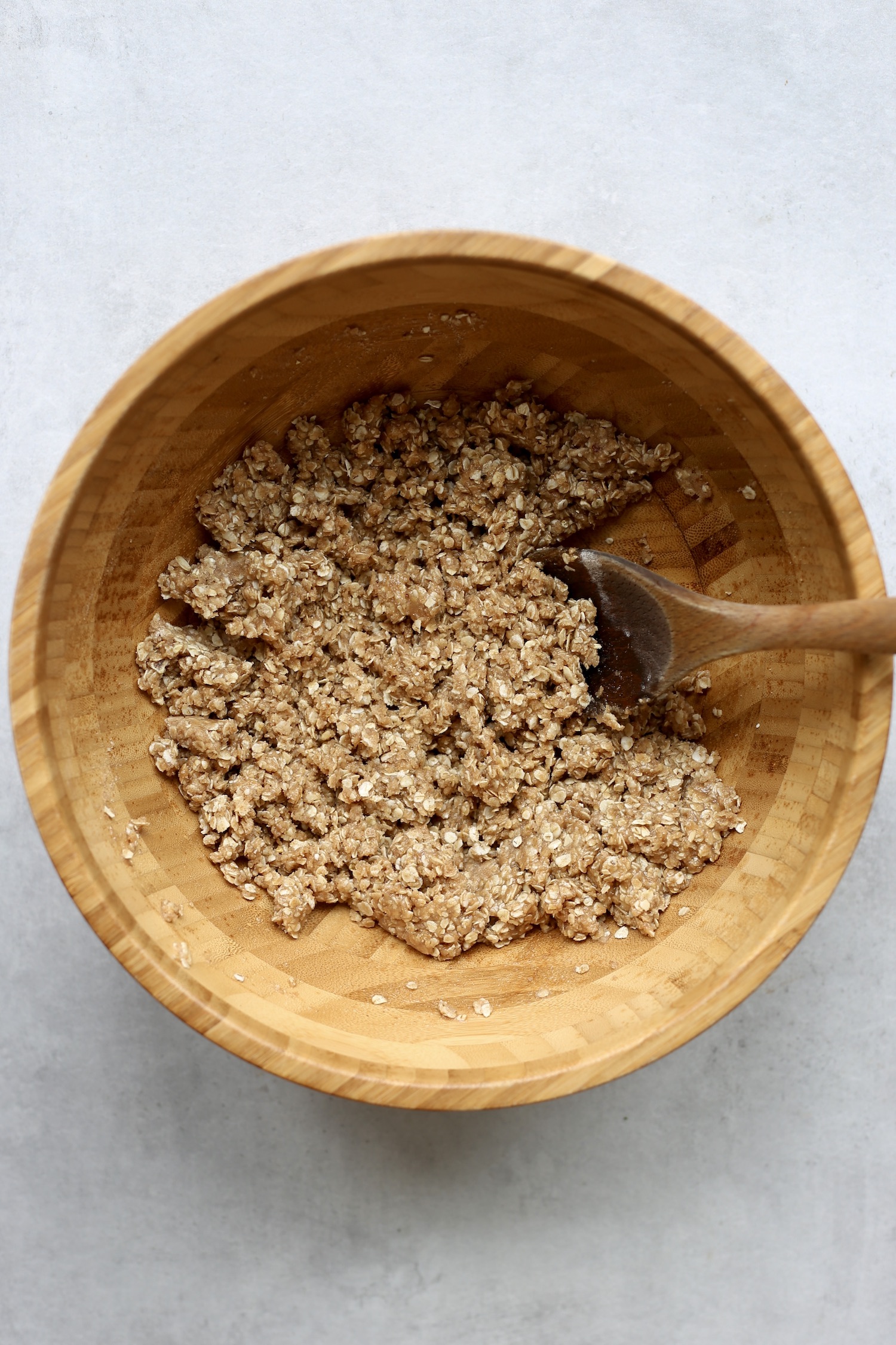 A wooden spoon is stirring together the dough for the vegan oatmeal bars. 