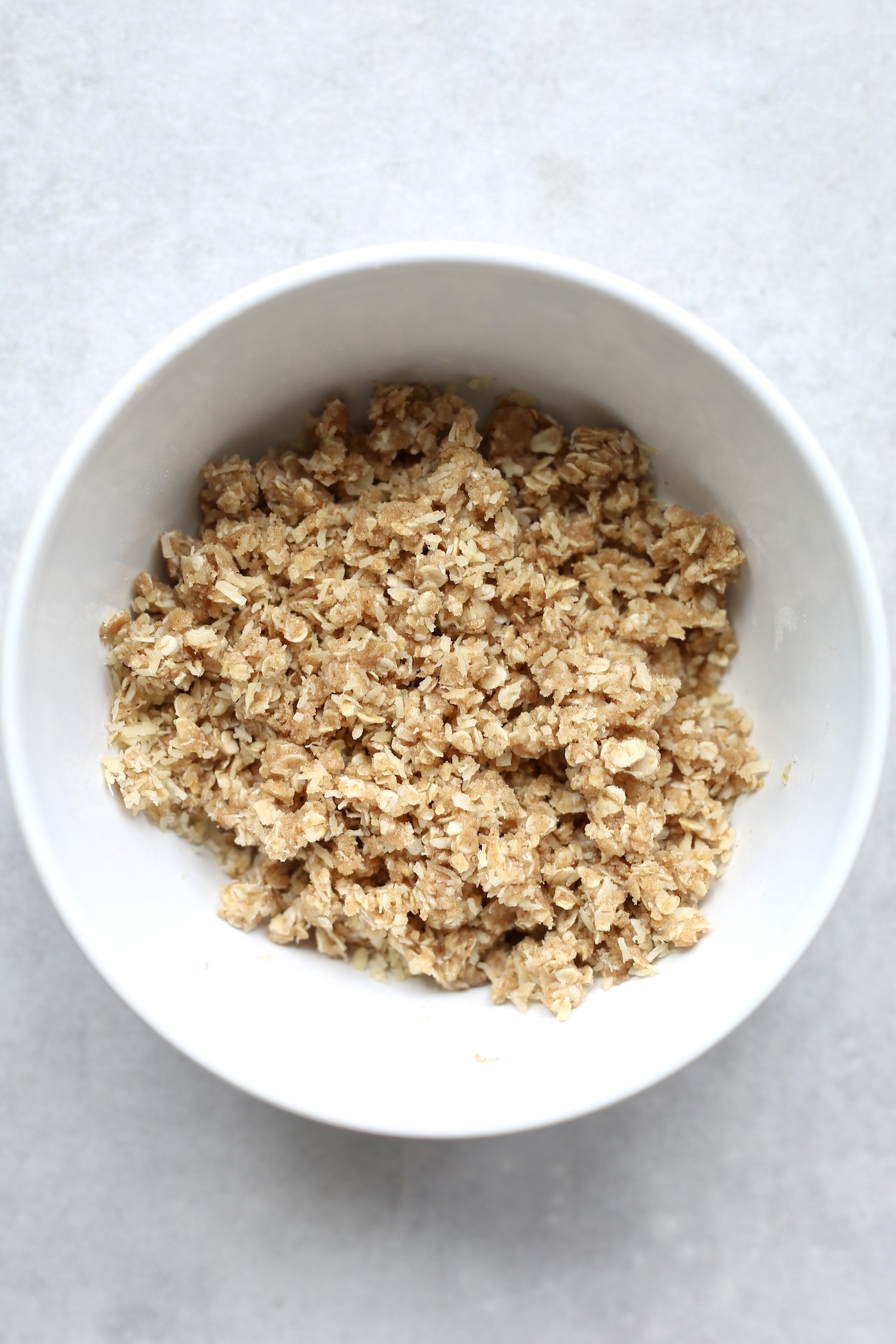 A white bowl filled with a mixture of oats, flour and coconut. 