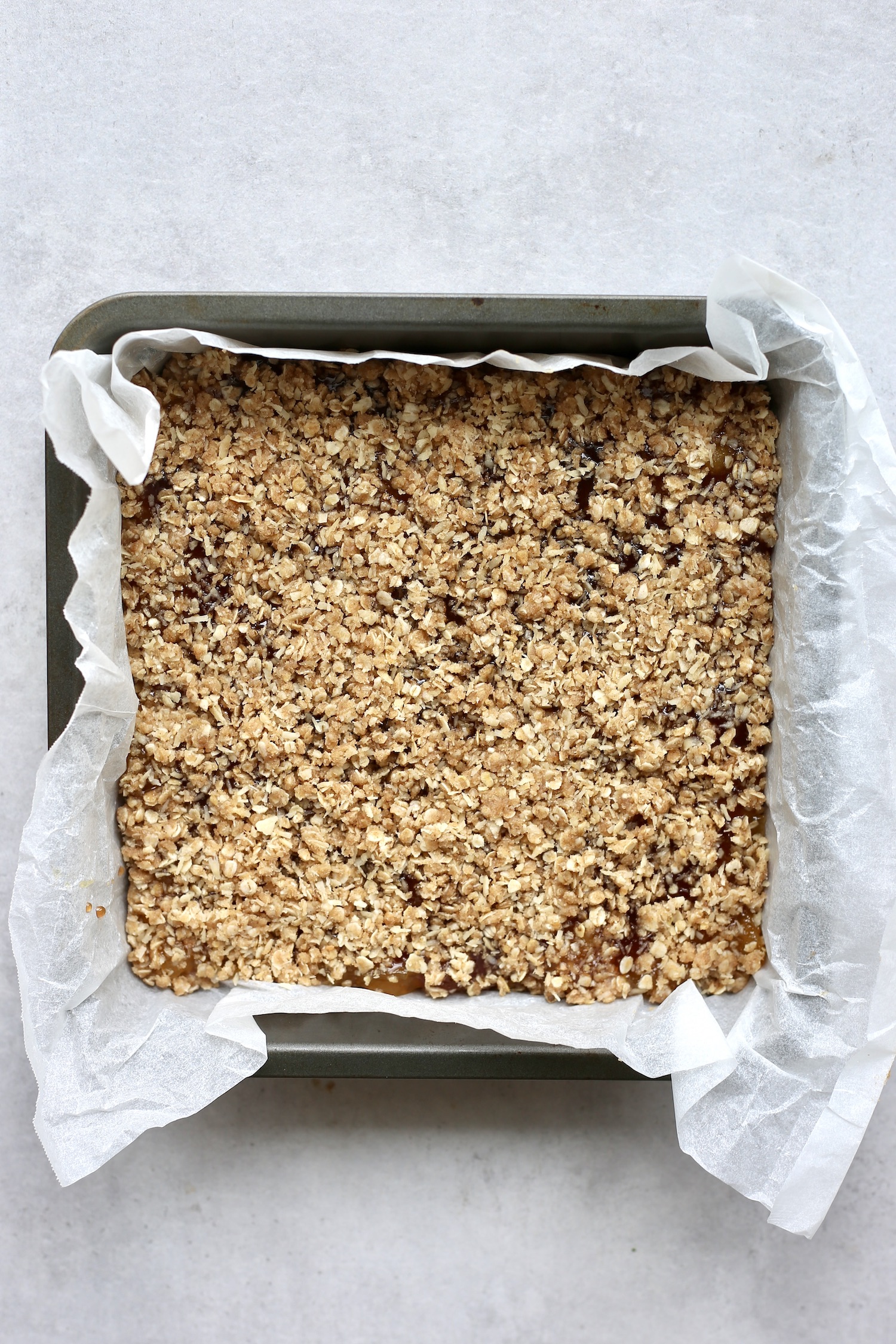 An overhead shot of vegan oatmeal bars in a parchment paper lined baking dish before baking. 