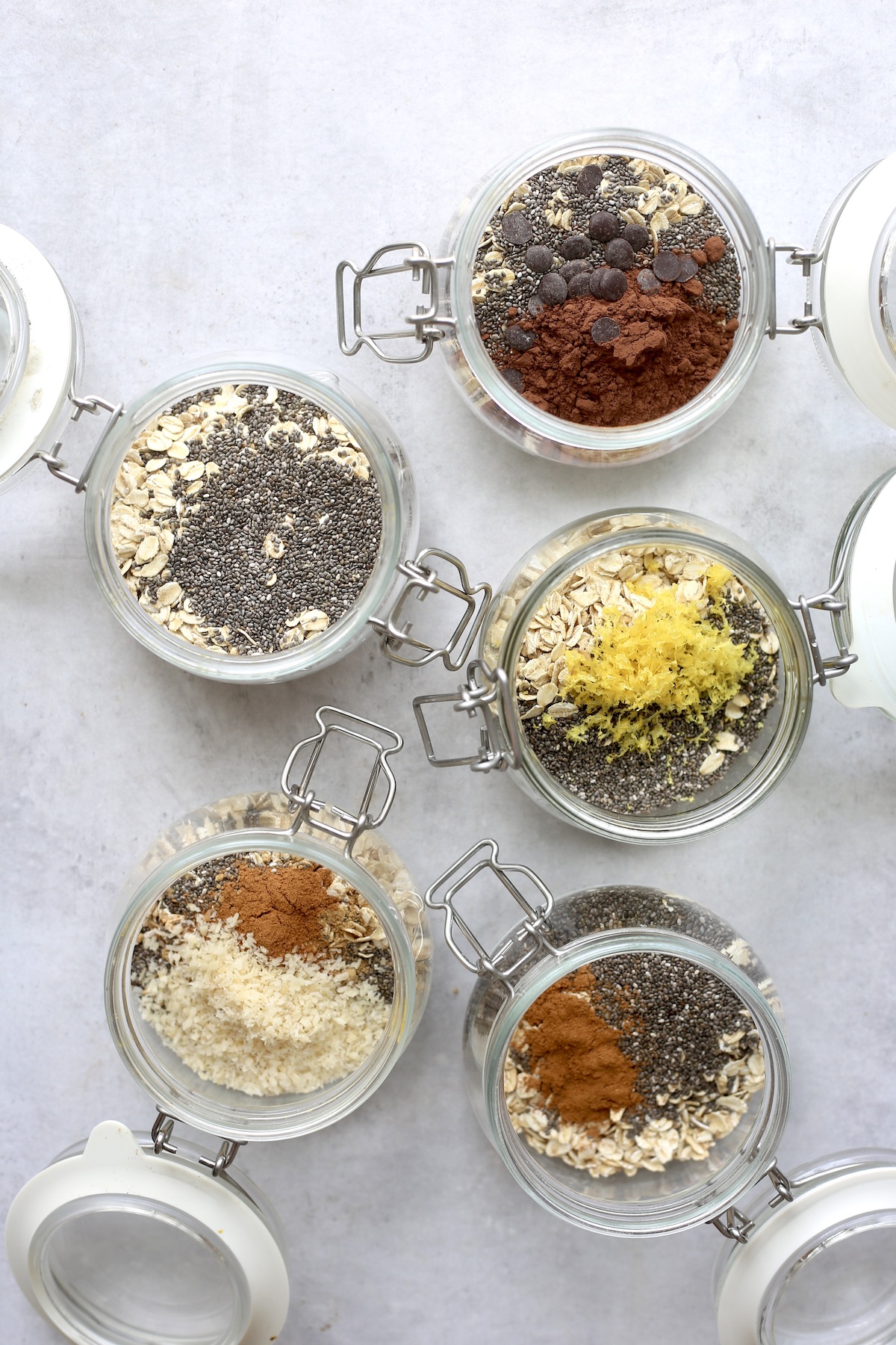 An overhead shot of 5 different swing top wide mouth jars filled with rolled oats, chia seeds and different flavorings. 