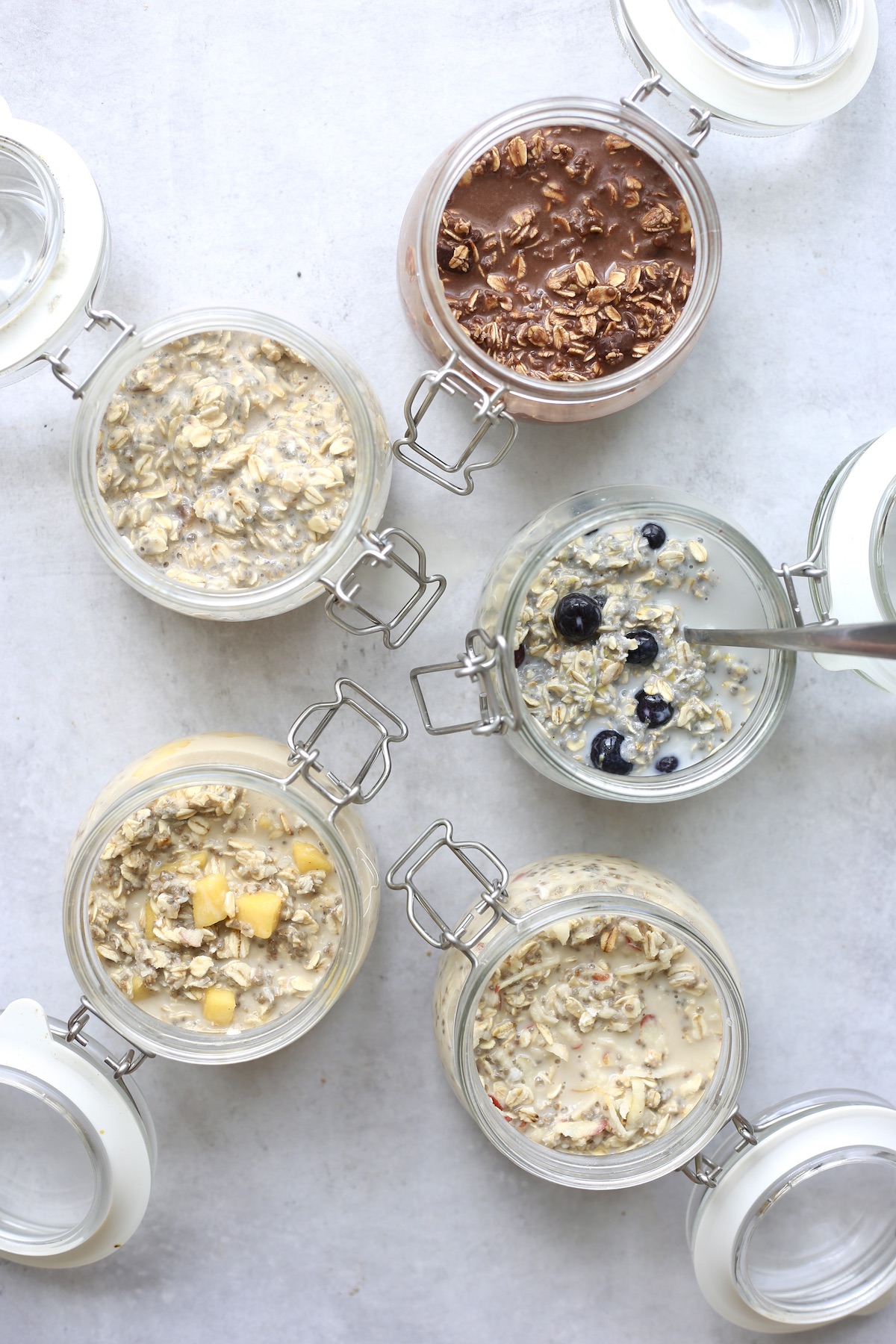 An overhead shot of five completed jars of different overnight oats flavors. 