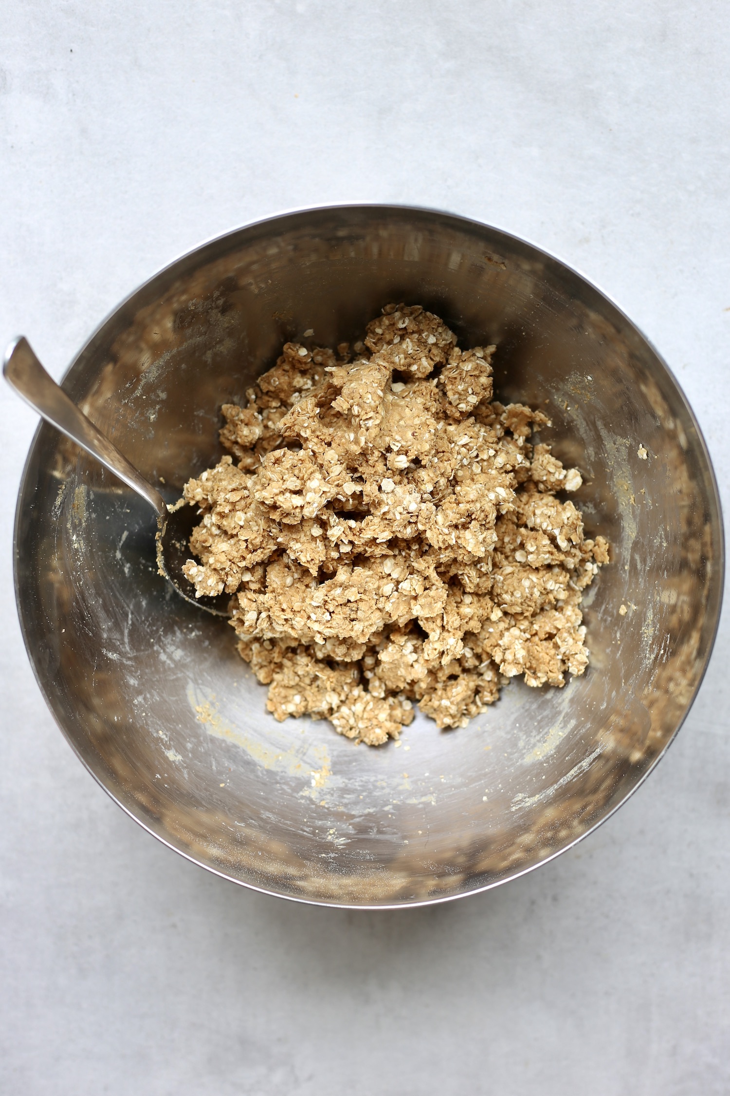 A spoon mixing together vegan protein ball dough in a large silver mixing bowl. 