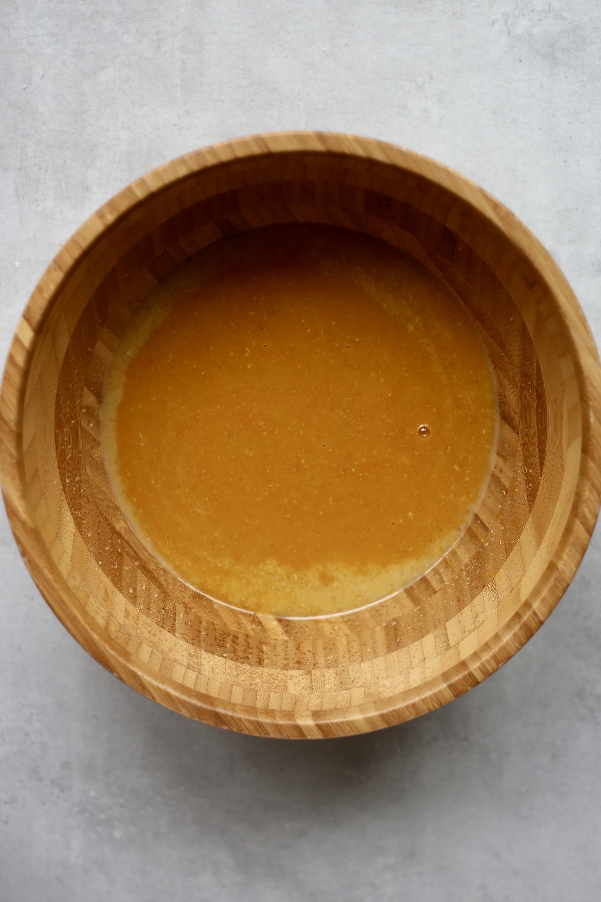 Pumpkin puree, oil and non-dairy milk mixed together in a large wooden mixing bowl.