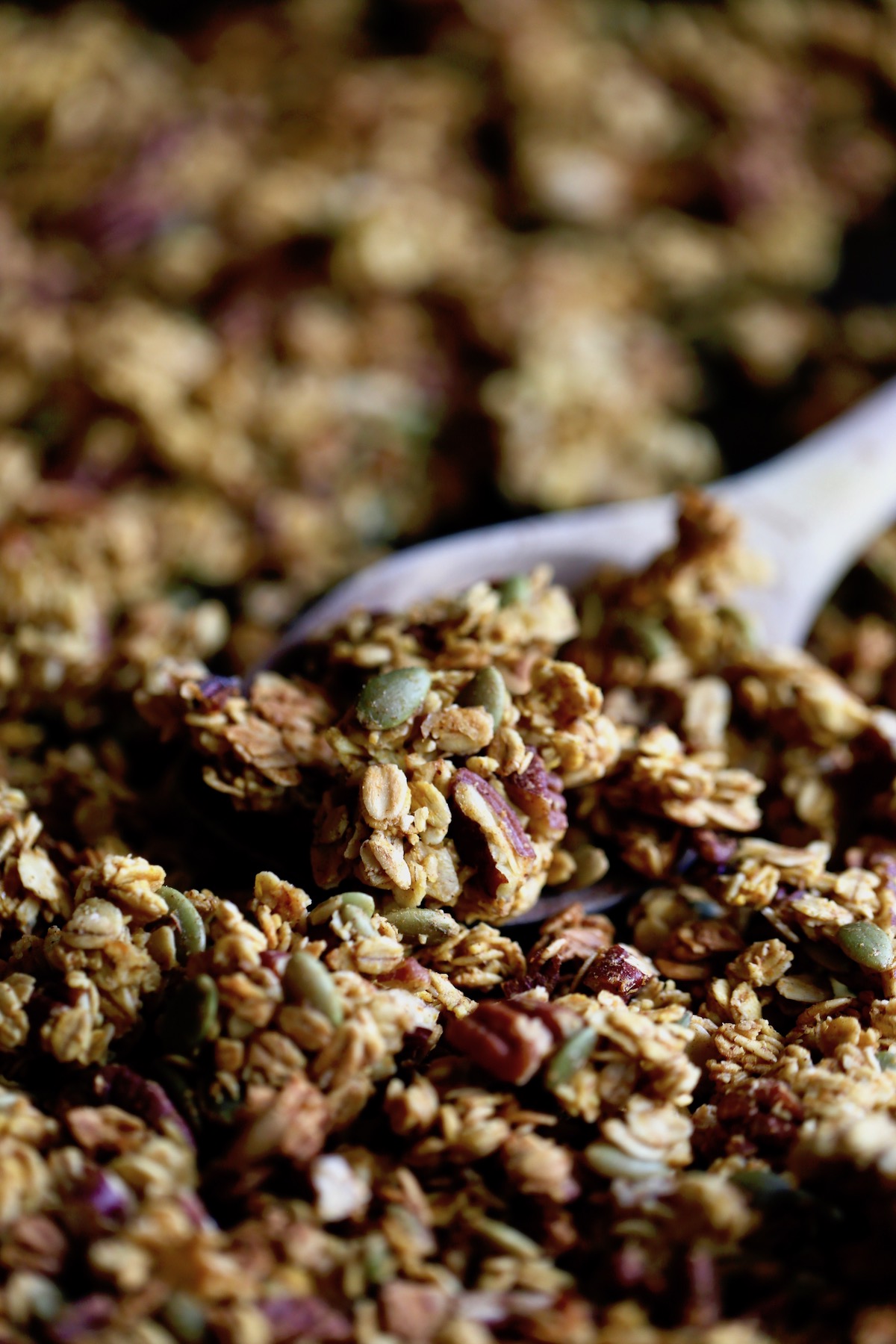 golden brown vegan pumpkin granola being scooped up with a wooden spoon