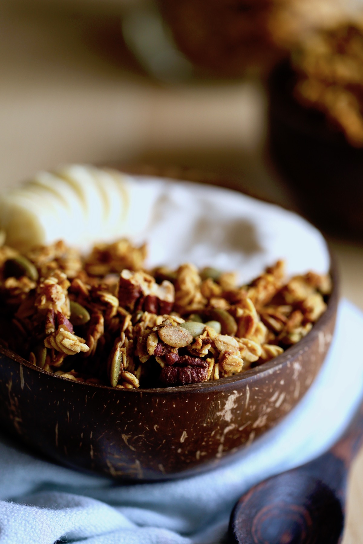 vegan pumpkin granola piled high in a coconut bowl with yogurt and banana