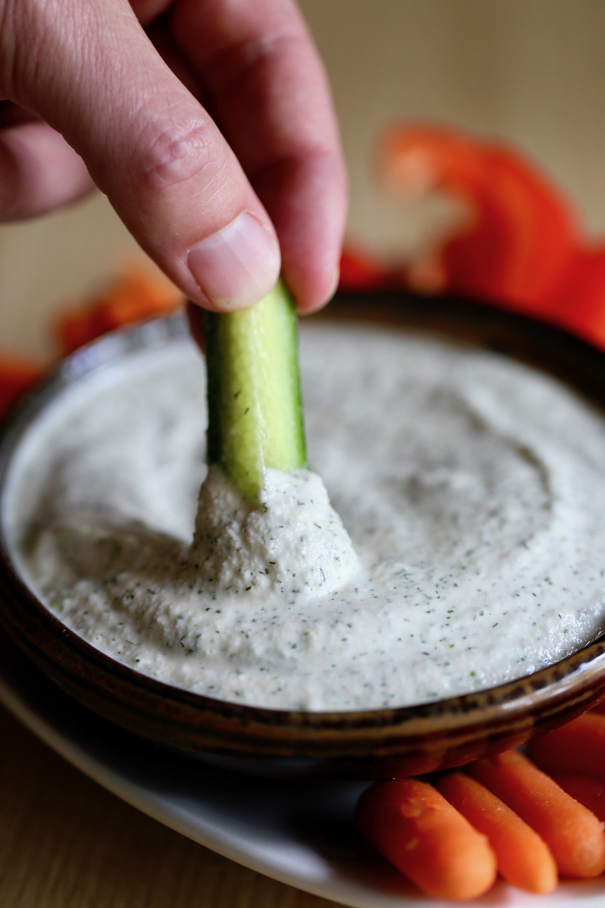 a cucumber being dipped into homemade cashew ranch dressing