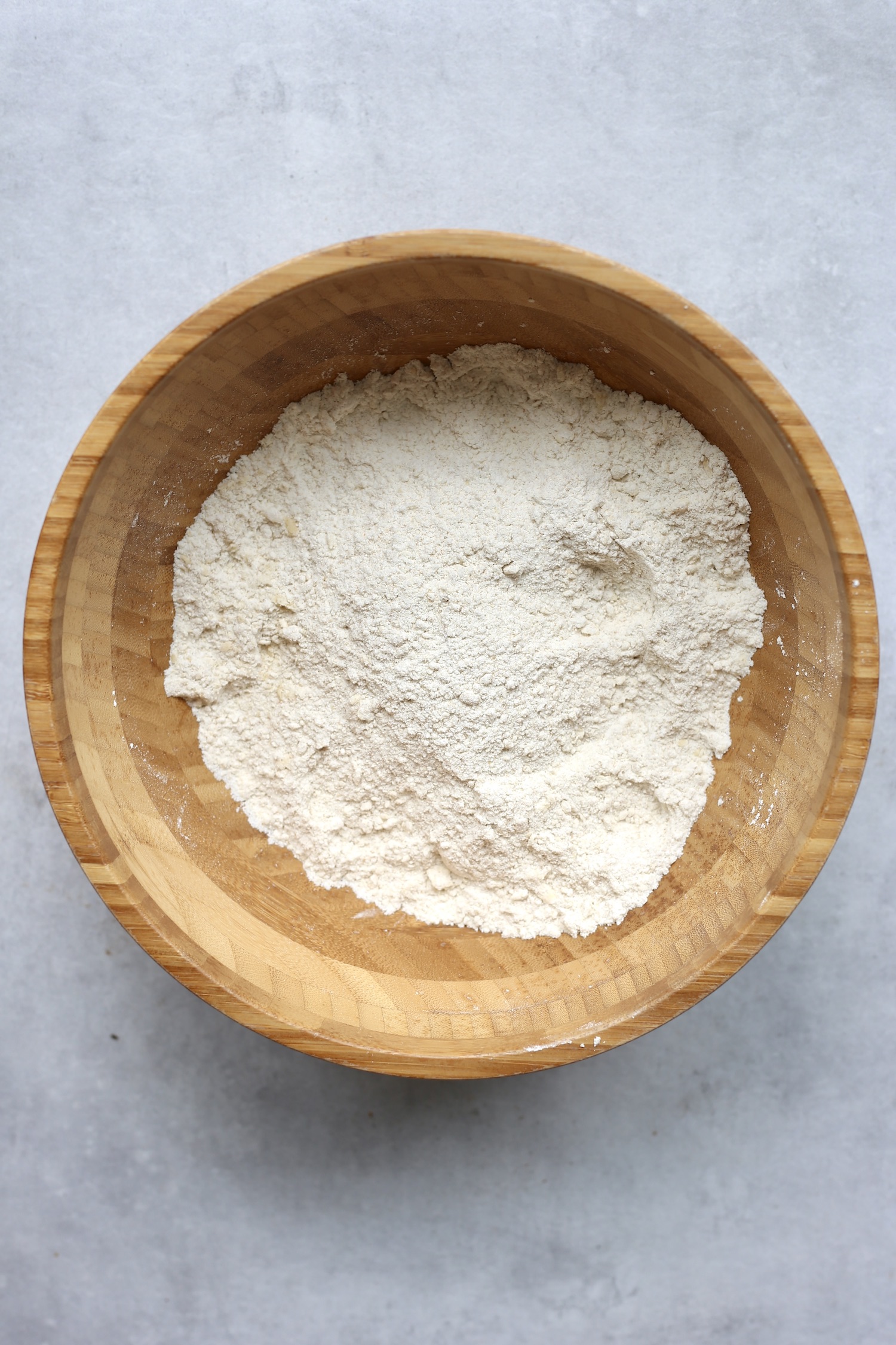 Vegan butter cut into flour until a sandy texture forms in a large wooden mixing board. 