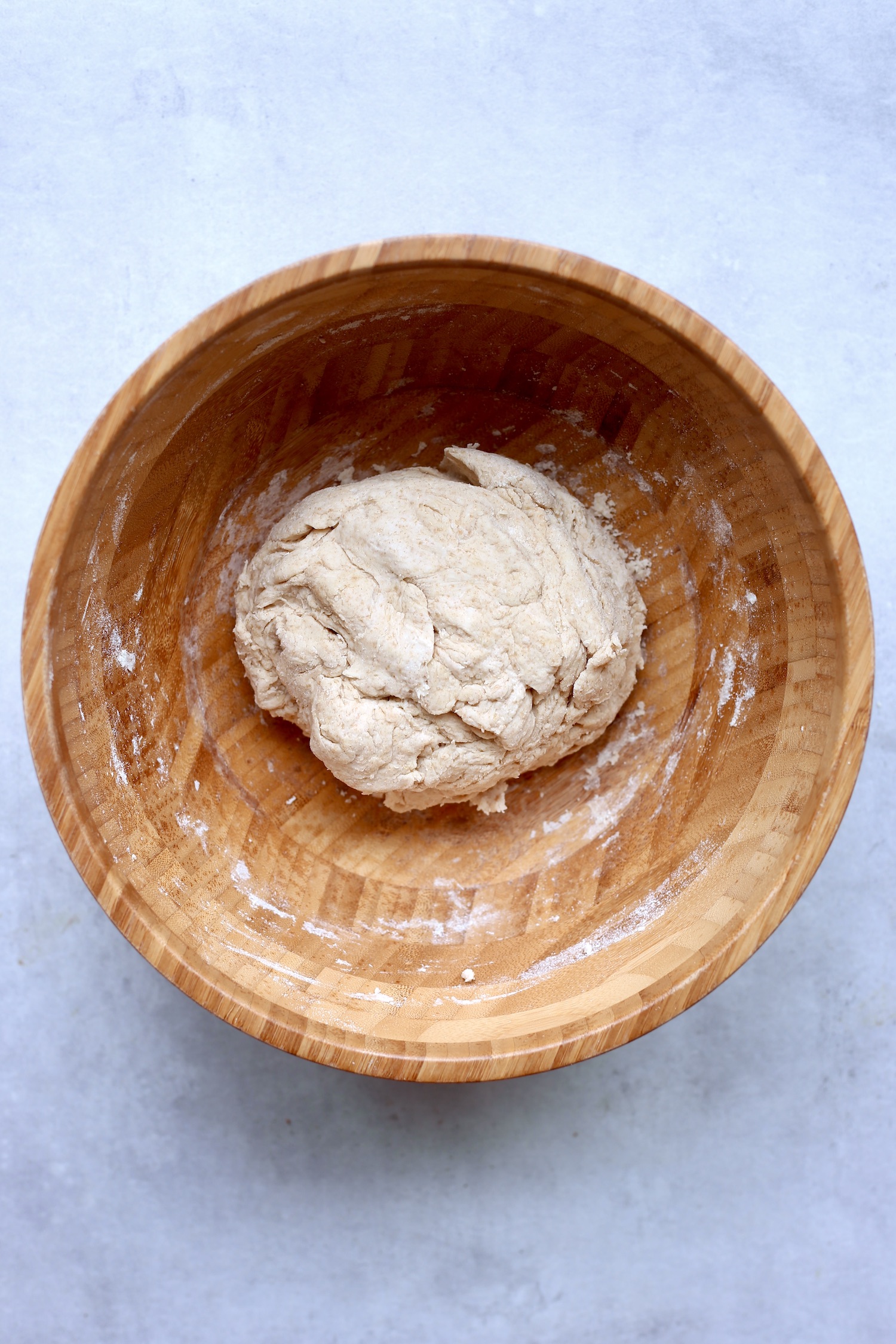 Shaggy vegan sourdough bread dough in a large wooden mixing bowl. 