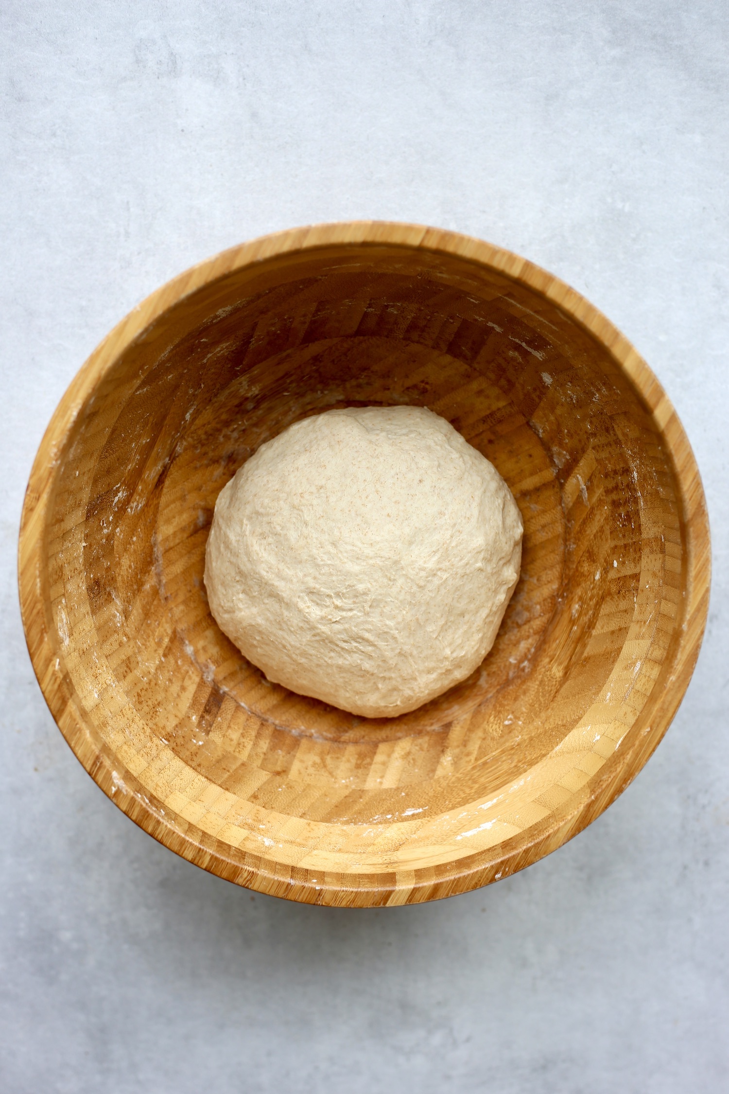 A smooth ball of dough resting in a large wooden mixing bowl. 