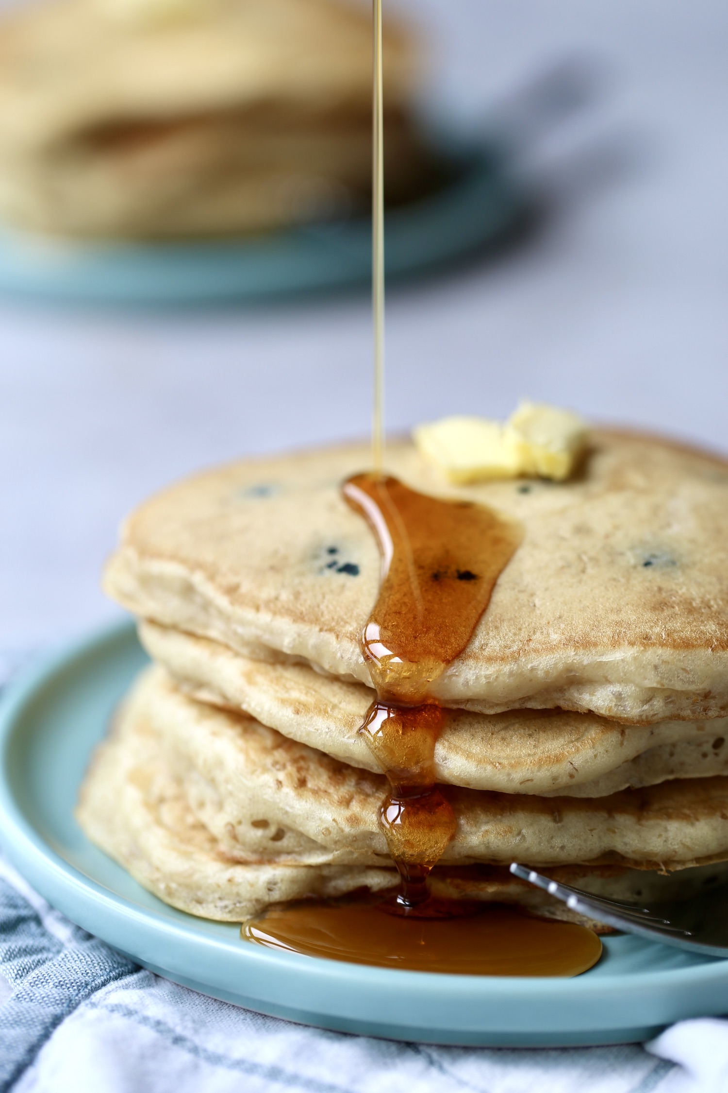 A thick stack of vegan sourdough pancakes on a blue plate being drizzled with maple syrup. 