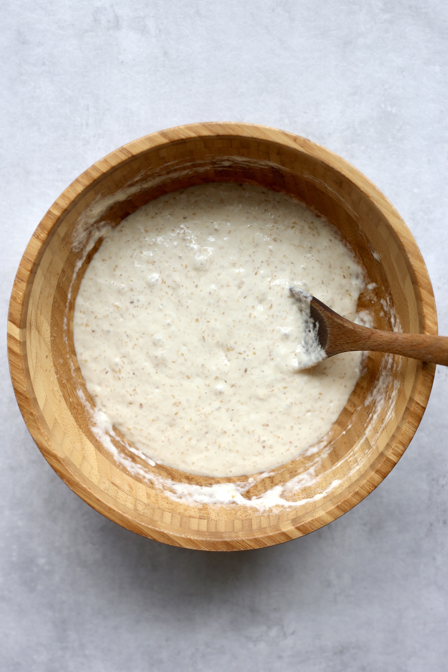 Fluffy, bubbly vegan pancake batter being stirred together in a wooden bowl with a wooden spoon. 