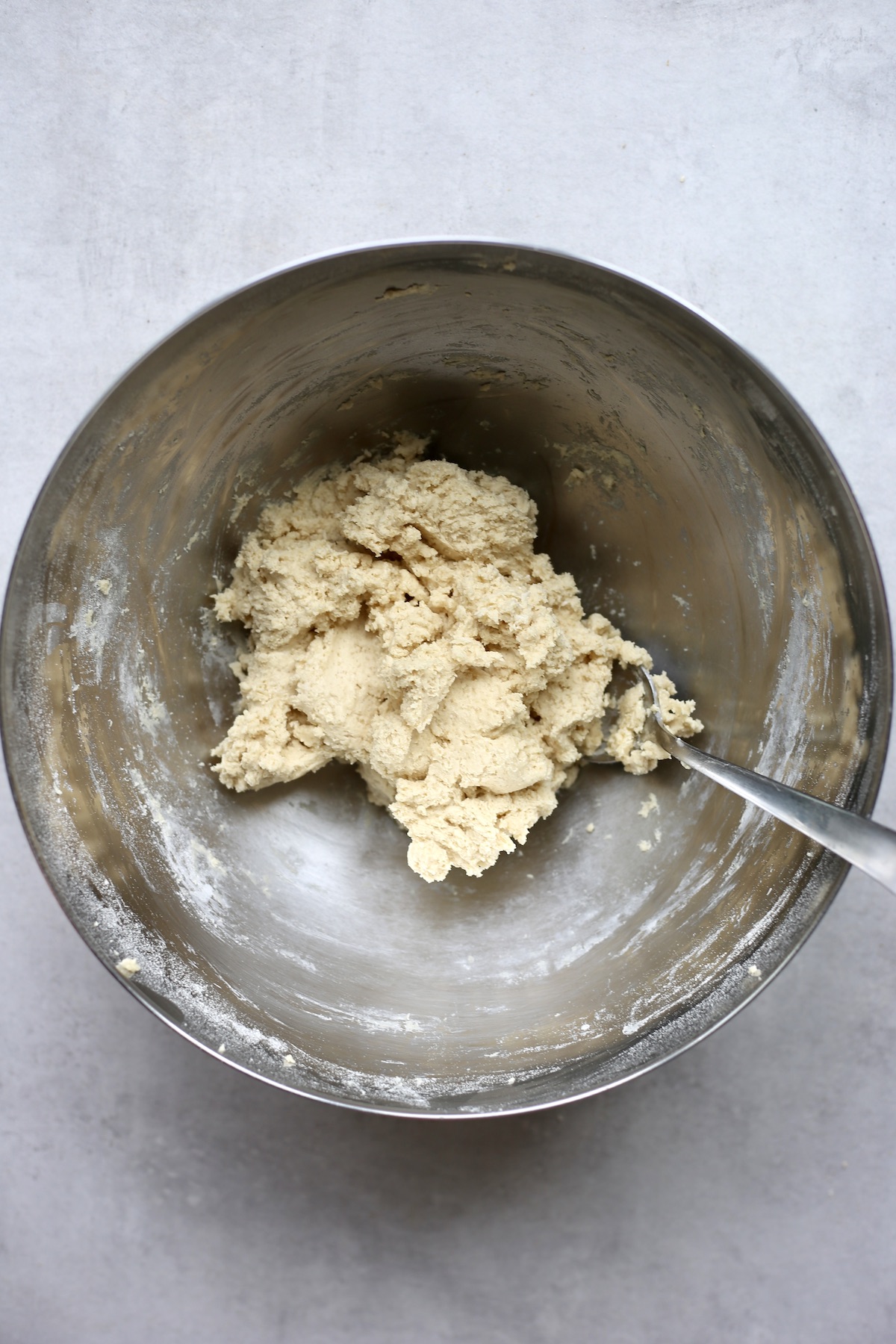 An overhead shot of vegan sugar cookie dough being stirred with a metal spoon in a silver mixing bowl.