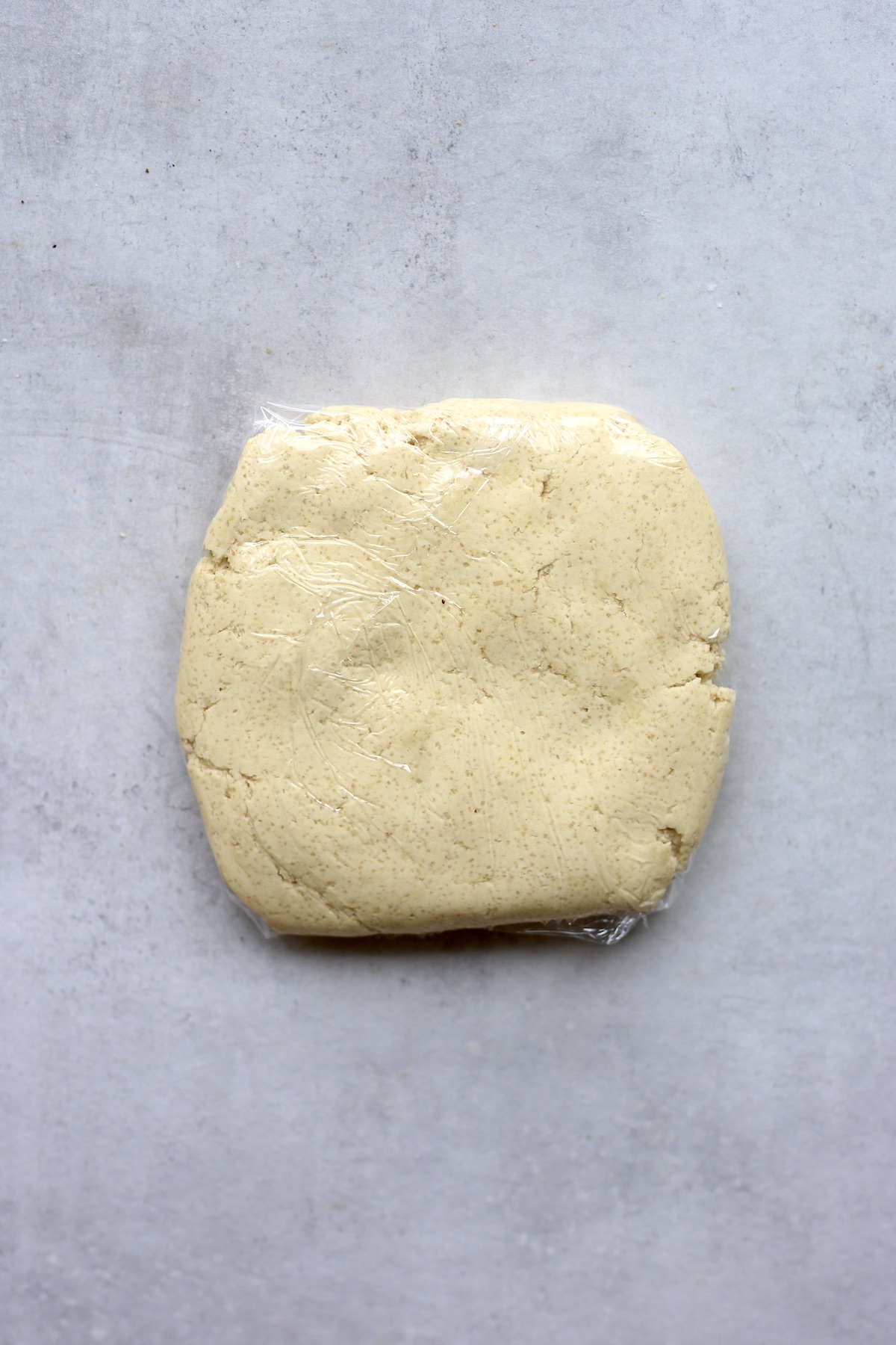 A square of vegan sugar cookie dough wrapped in plastic wrap. 