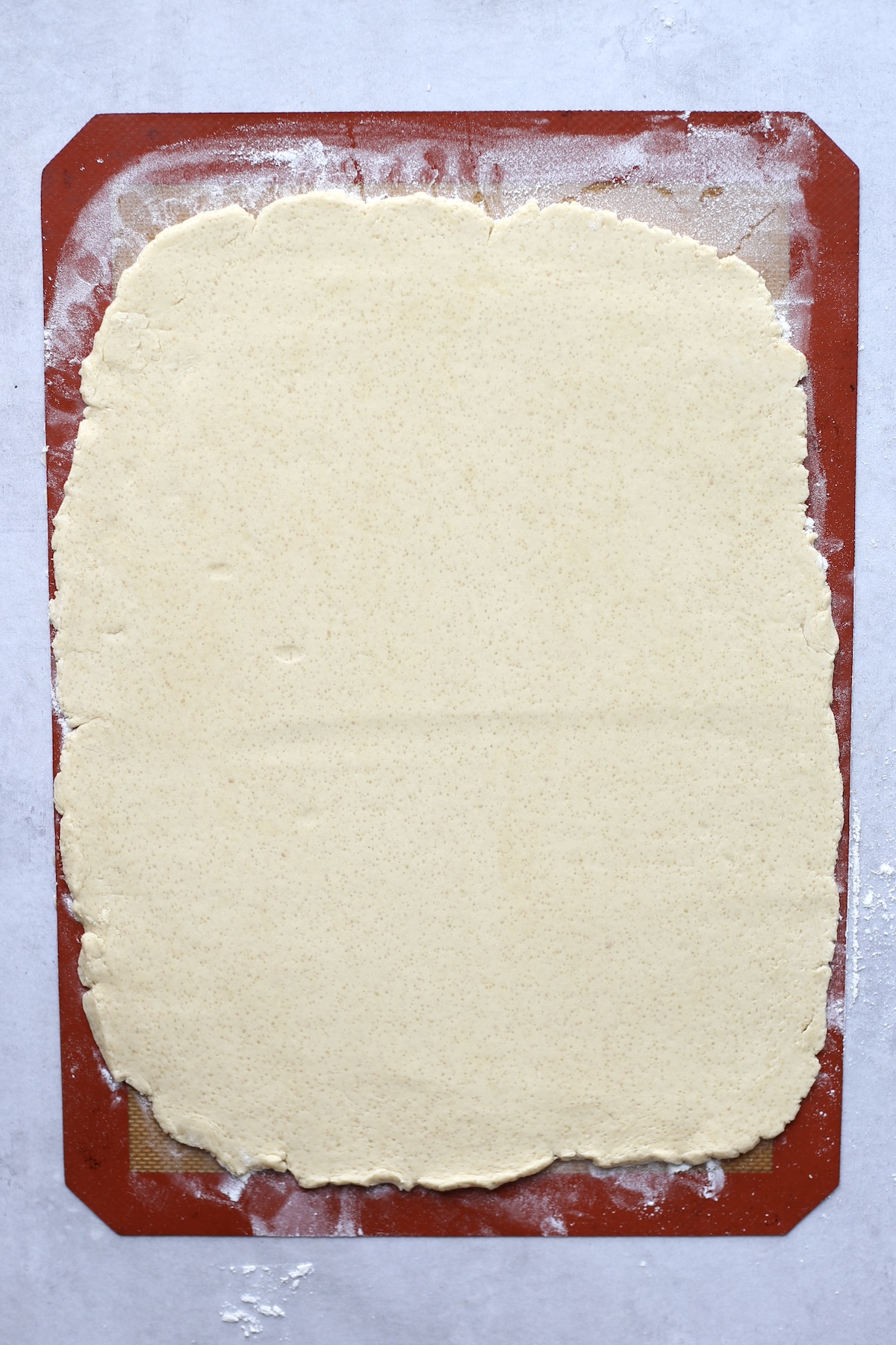 A large rectangle of vegan sugar cookie dough rolled out on a silicone baking mat. 