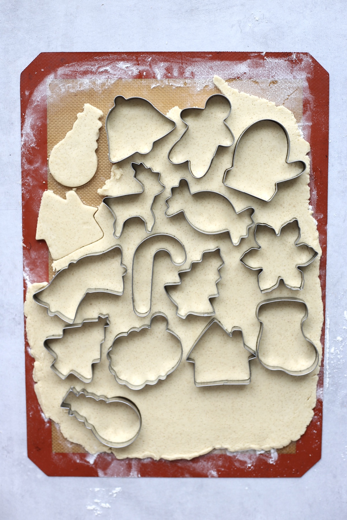 Silver Christmas cookie cutters pressed into a large sheet of sugar cookie dough.