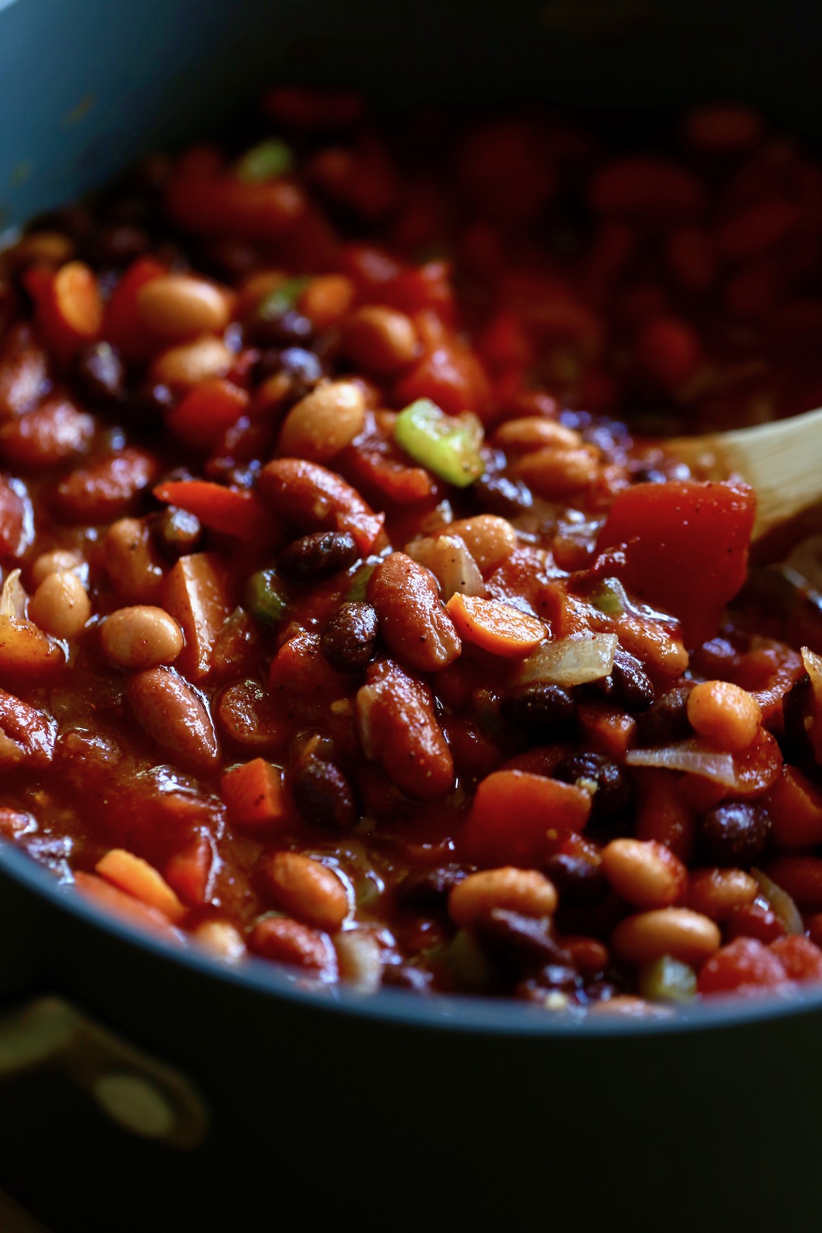 vegan three bean chili being stirred in a pot with a wooden spoon