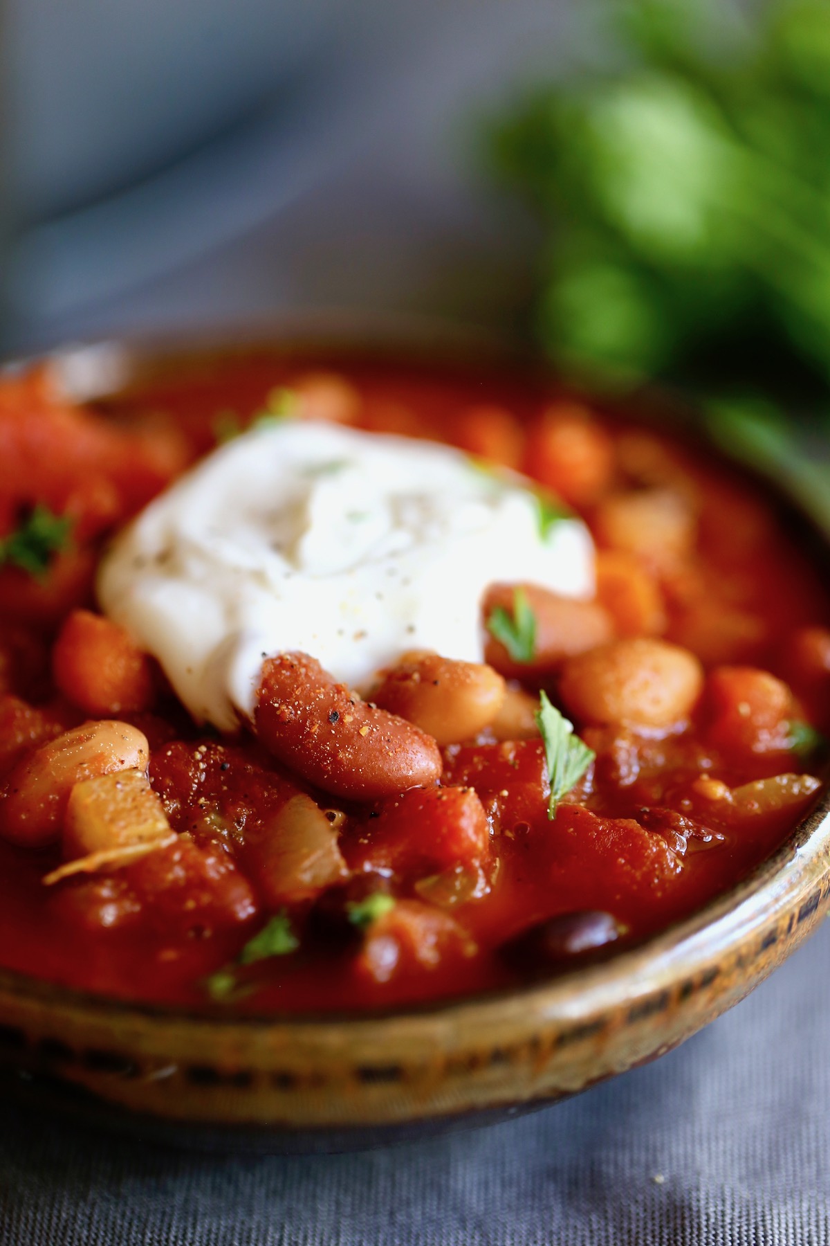 three bean chili in a bowl topped with vegan sour cream and fresh parsley