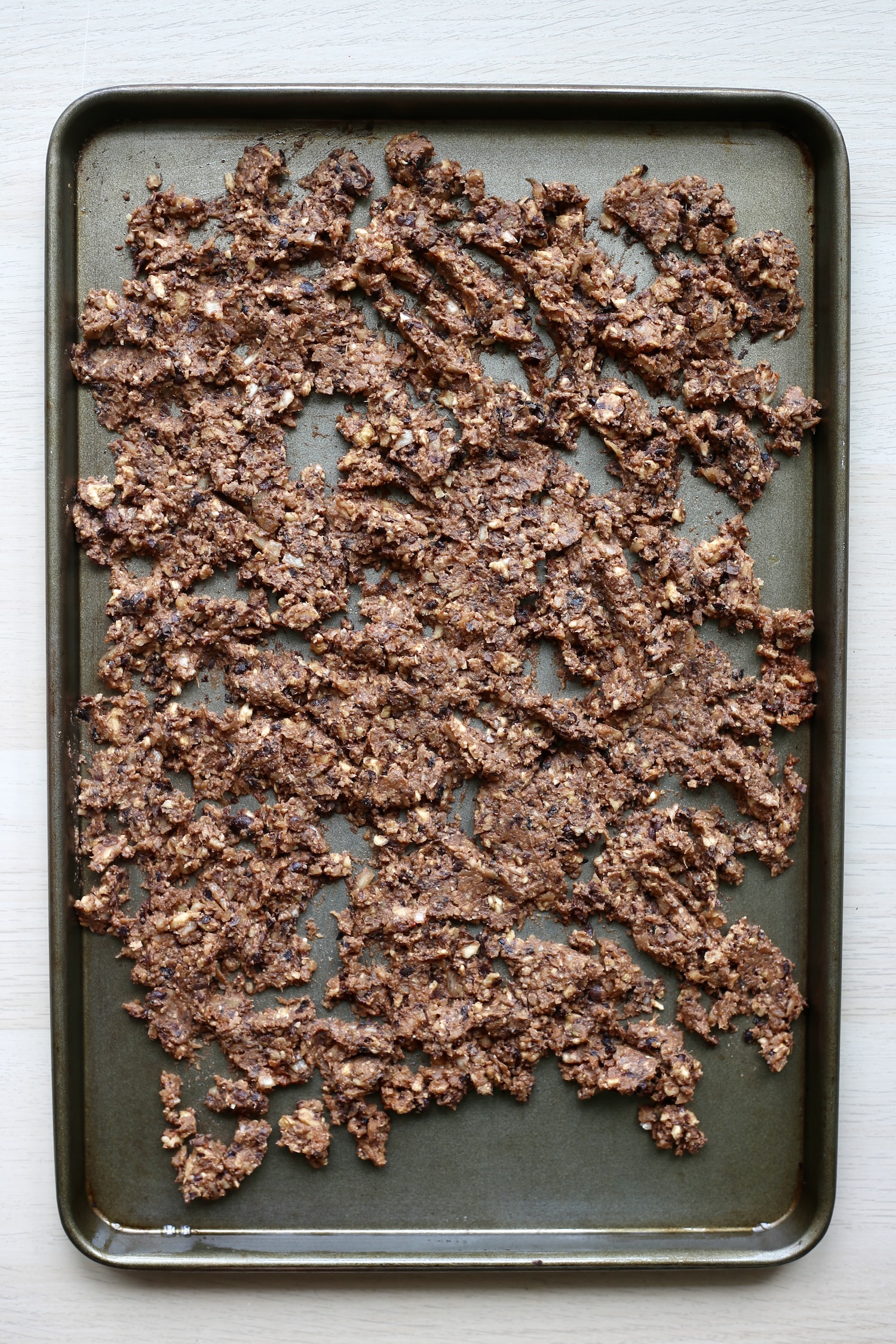 Un-cooked walnut vegan taco meat spread out on a baking sheet. 