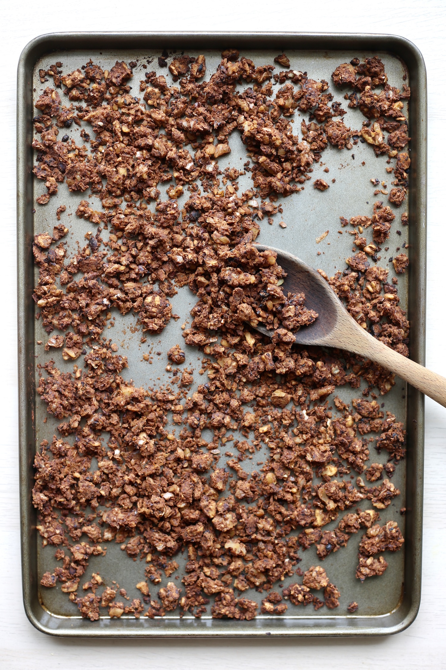 A wooden spoon scooping up crumbly walnut taco meat on a baking dish. 