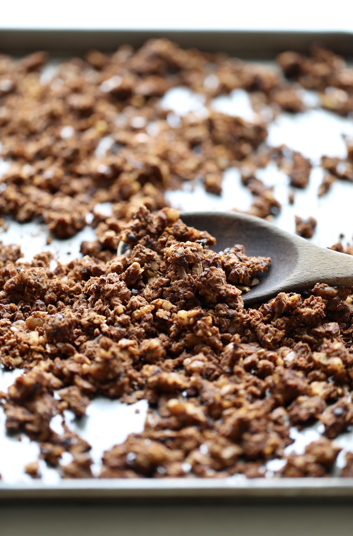 A wooden spoon scooping up some vegan walnut taco meat from a baking sheet. 