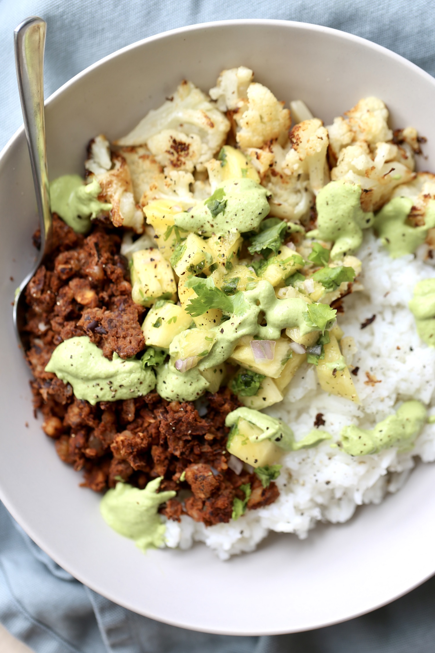 An overhead shot of walnut taco meat paired with white rice, pineapple salsa, cilantro lime sauce and fresh cilantro in a large bowl.