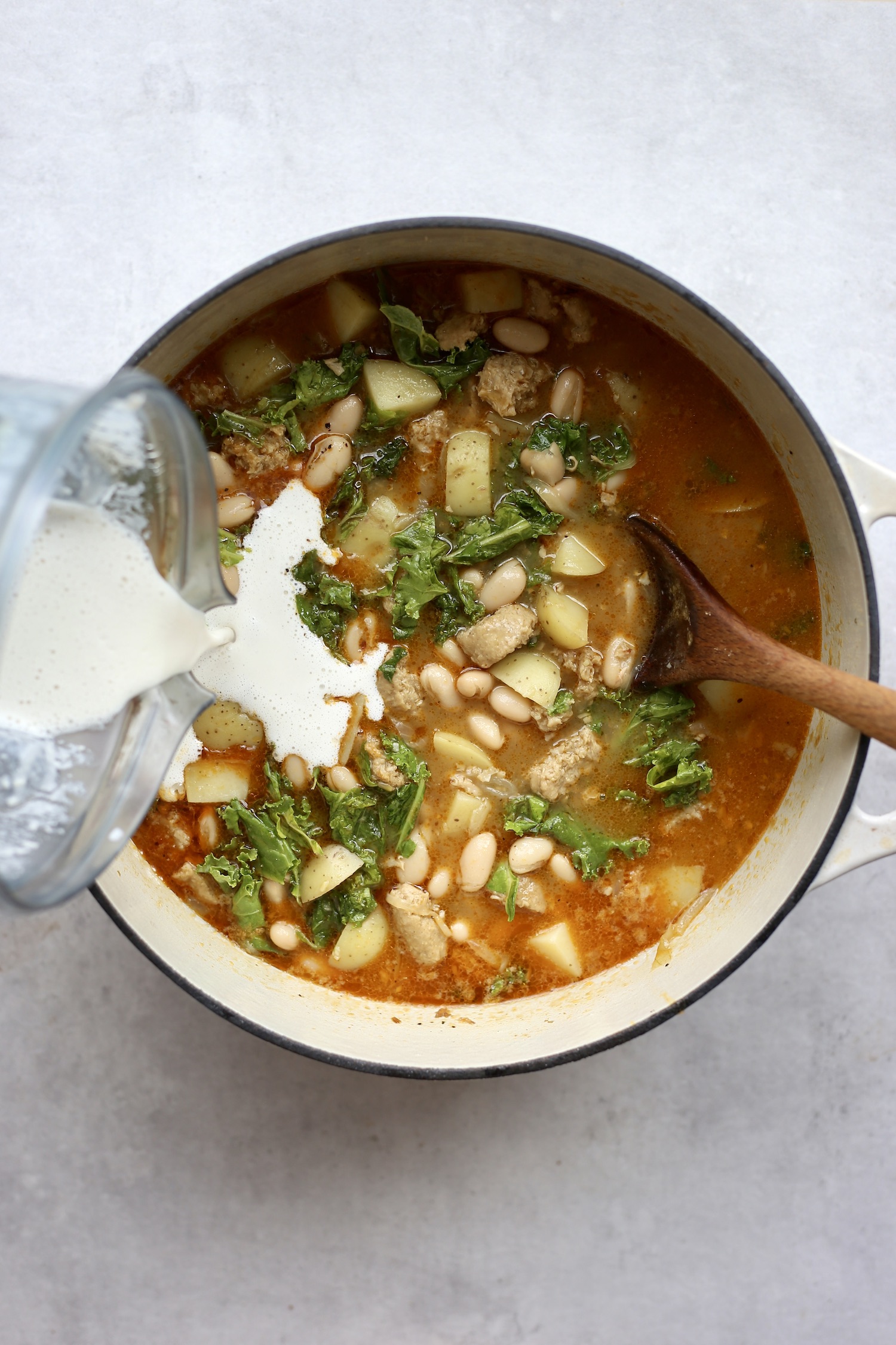 Cashew cream being poured into vegan zuppa toscana. 