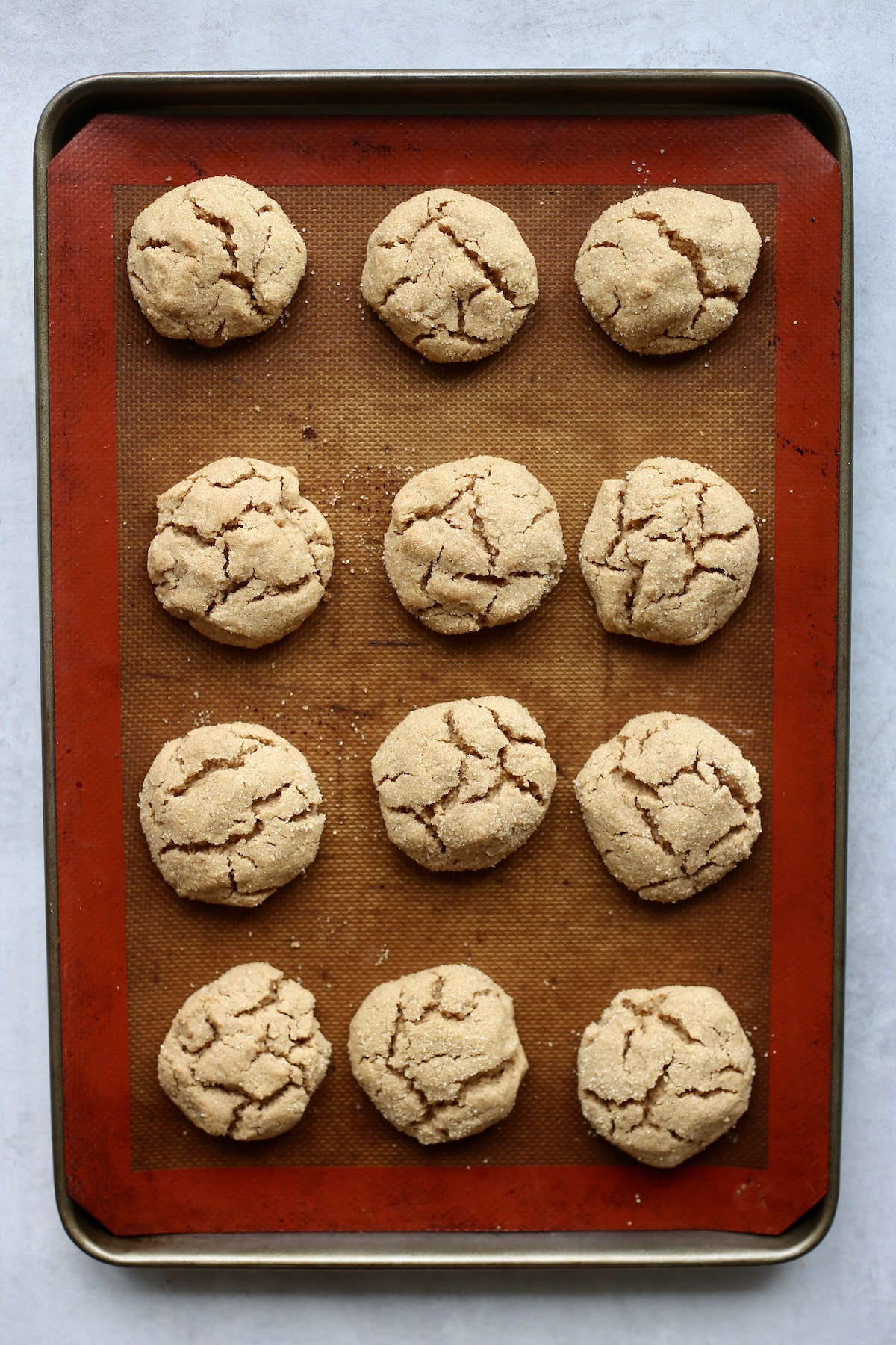 An overhead shot of 12 cracked vegan peanut butter cookies just after baking on a silicone lined baking sheet.