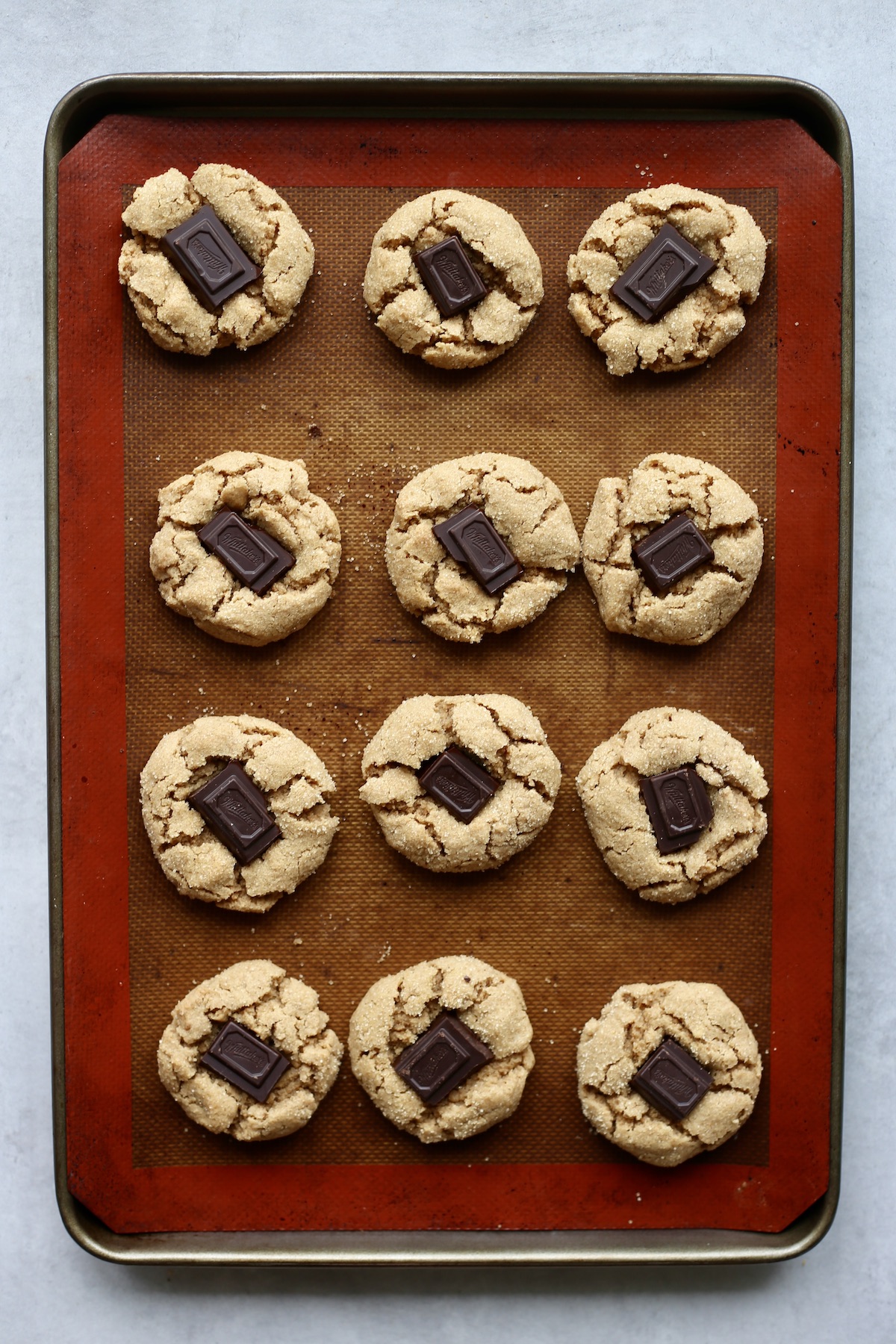 An overhead shot of 12 vegan peanut butter blossoms on a silicone lined baking sheet. 