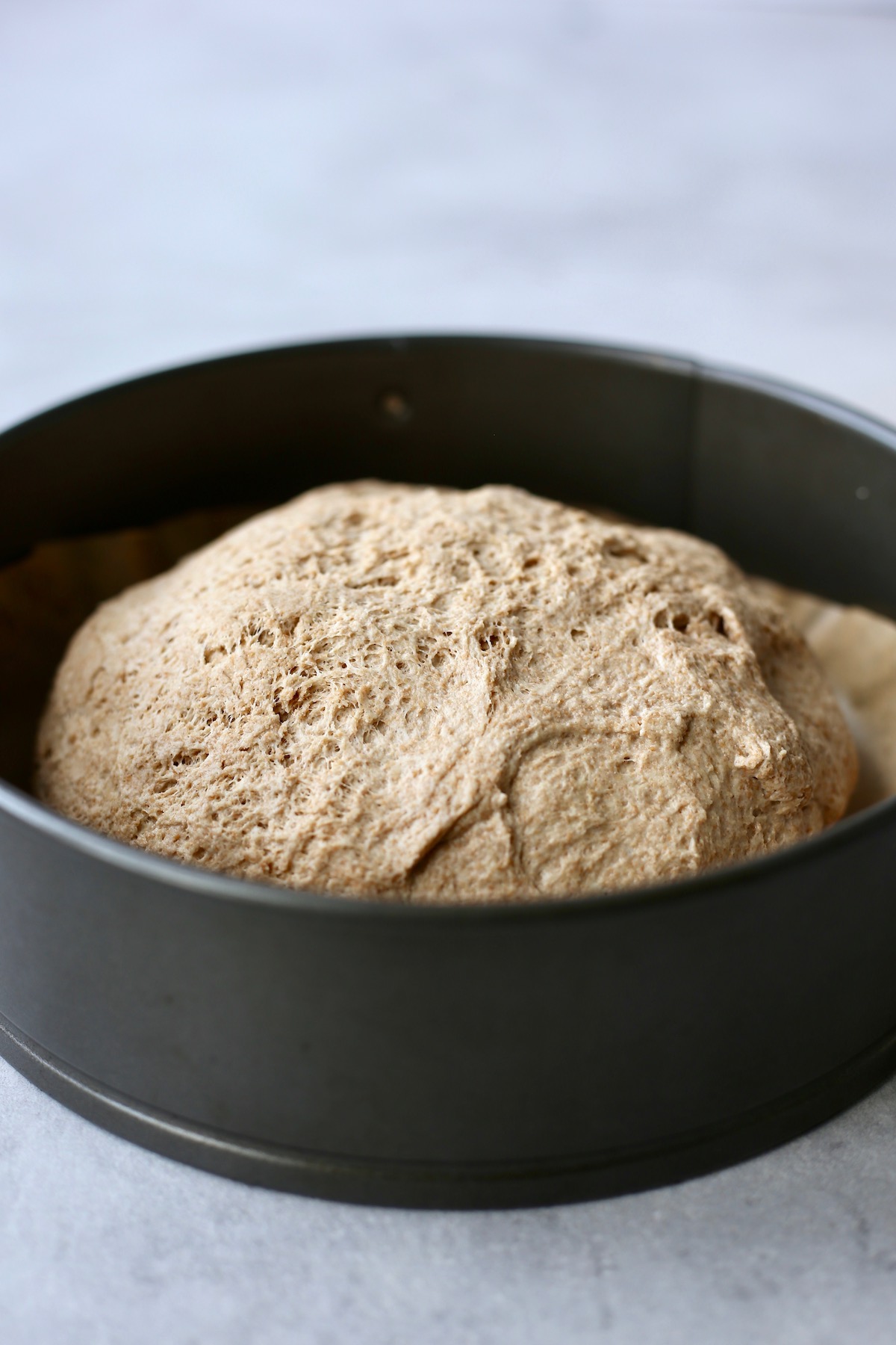 A large ball of whole wheat dough in a black cake pan.